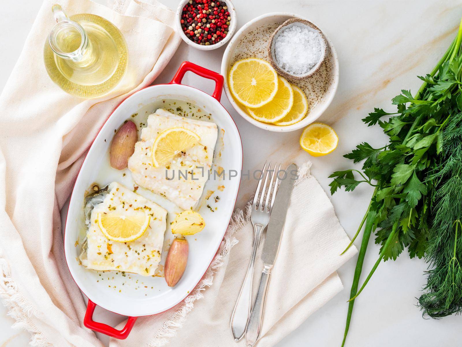 cod fish fillet, freshly cooked in oven with onion in porcelain dish for baking, lemon on plate by NataBene