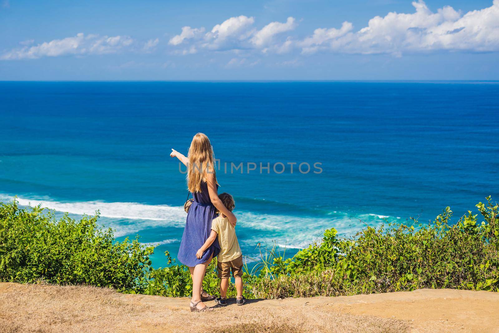 Mom and son travelers on a cliff above the beach. Empty paradise beach, blue sea waves in Bali island, Indonesia. Suluban and Nyang Nyang place. Traveling with kids concept.