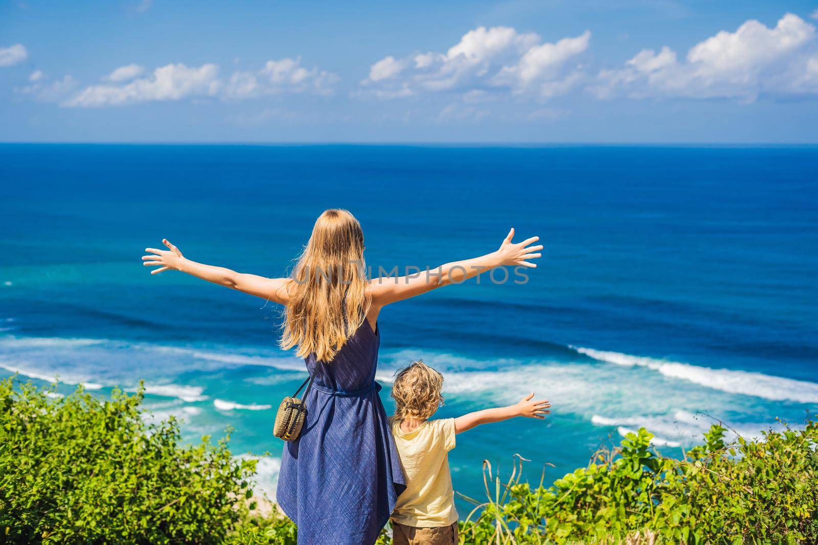 Mom and son travelers on a cliff above the beach. Empty paradise beach, blue sea waves in Bali island, Indonesia. Suluban and Nyang Nyang place. Traveling with kids concept.