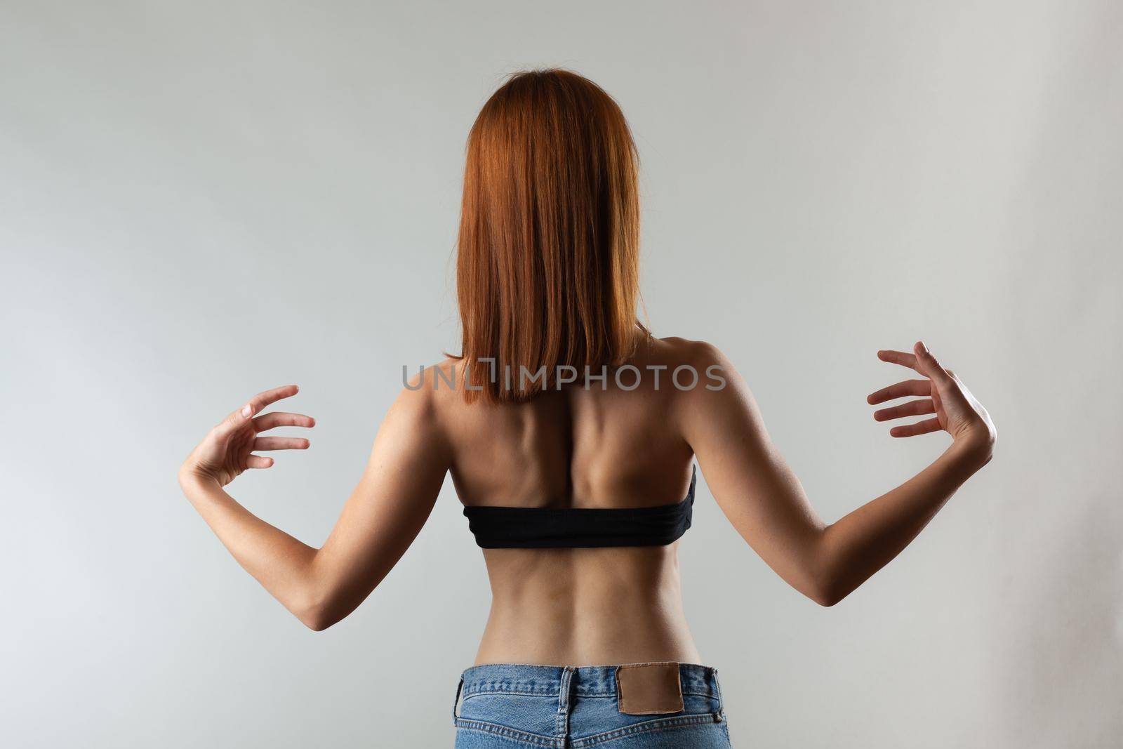 Beautiful girl with burnt orange hair stretching and making ballet pose. Studio portrait on gray background.