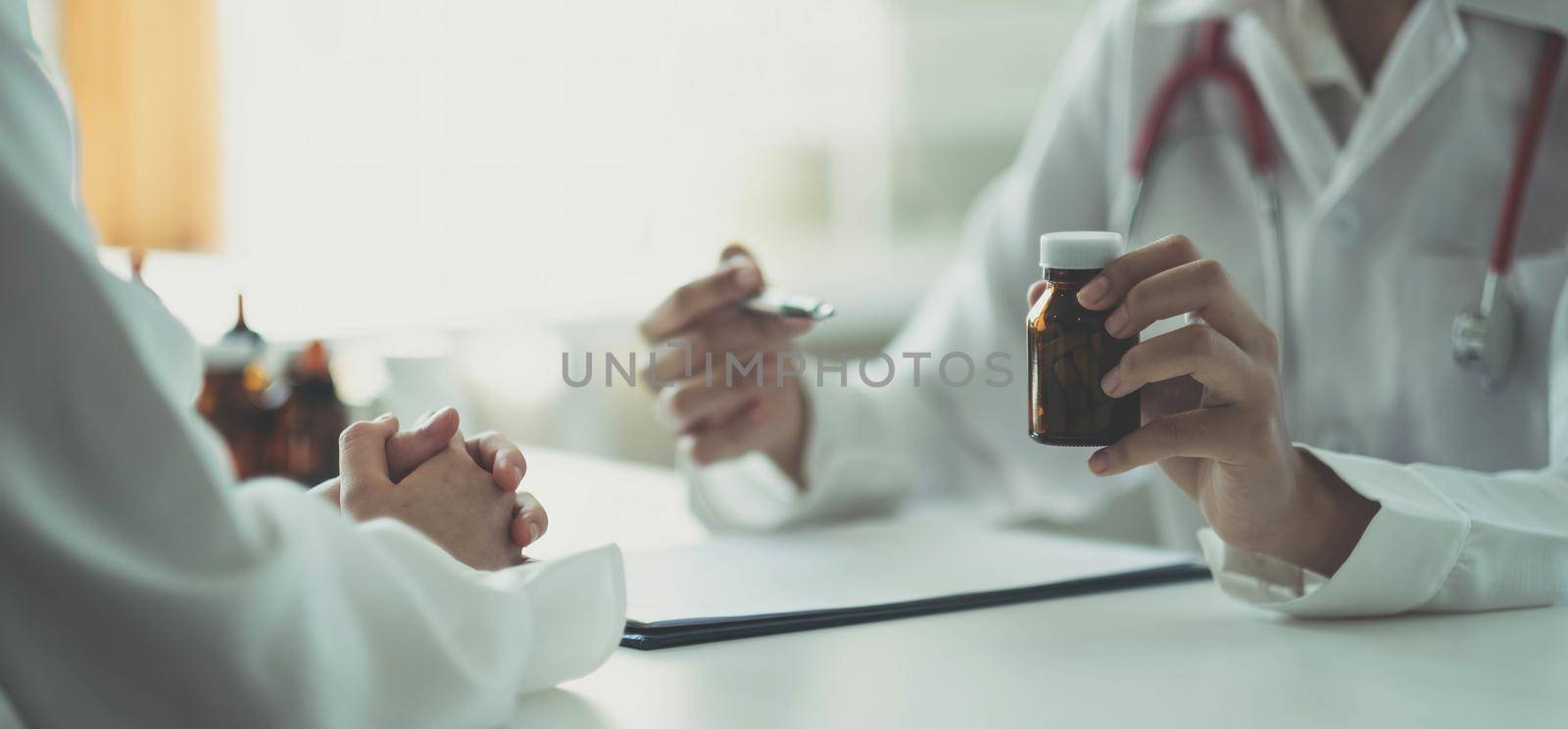 The doctor and the patient talked about something while sitting at the table. A doctor holds a bottle of medicine explaining in detail the kind of medicine.