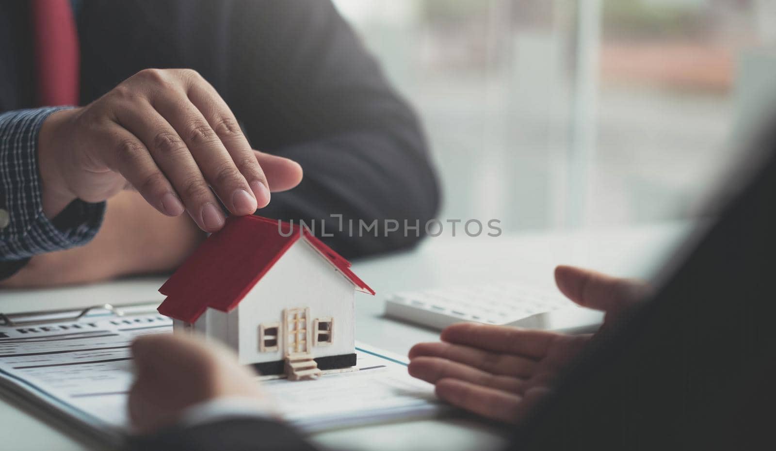 The real estate agent is explaining the house style to the clients who come to contact to see the house design and the purchase agreement. Within a modern office.