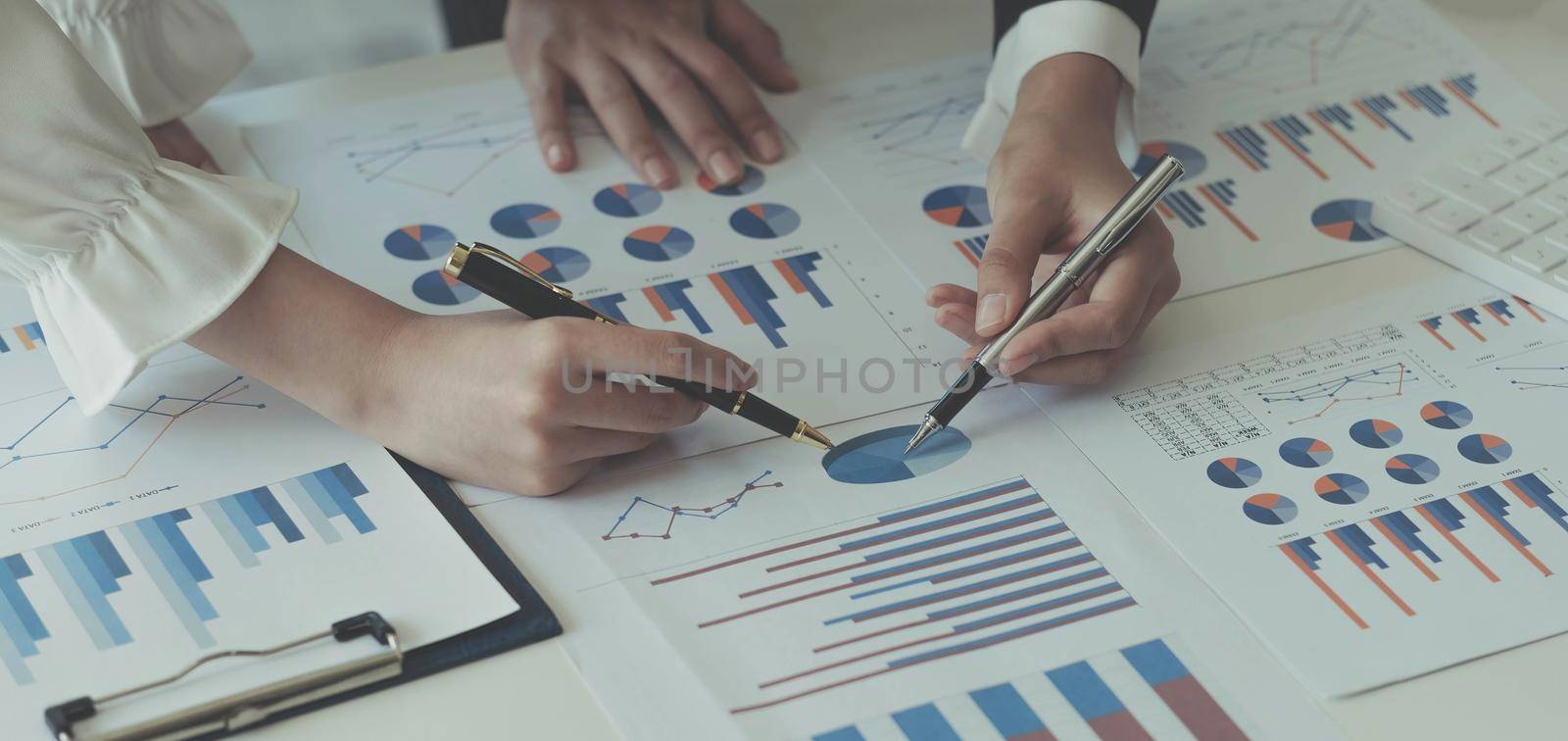 Close-up of two women's hands pointing to a turnover chart while talking on a wooden table in the office. group support concept