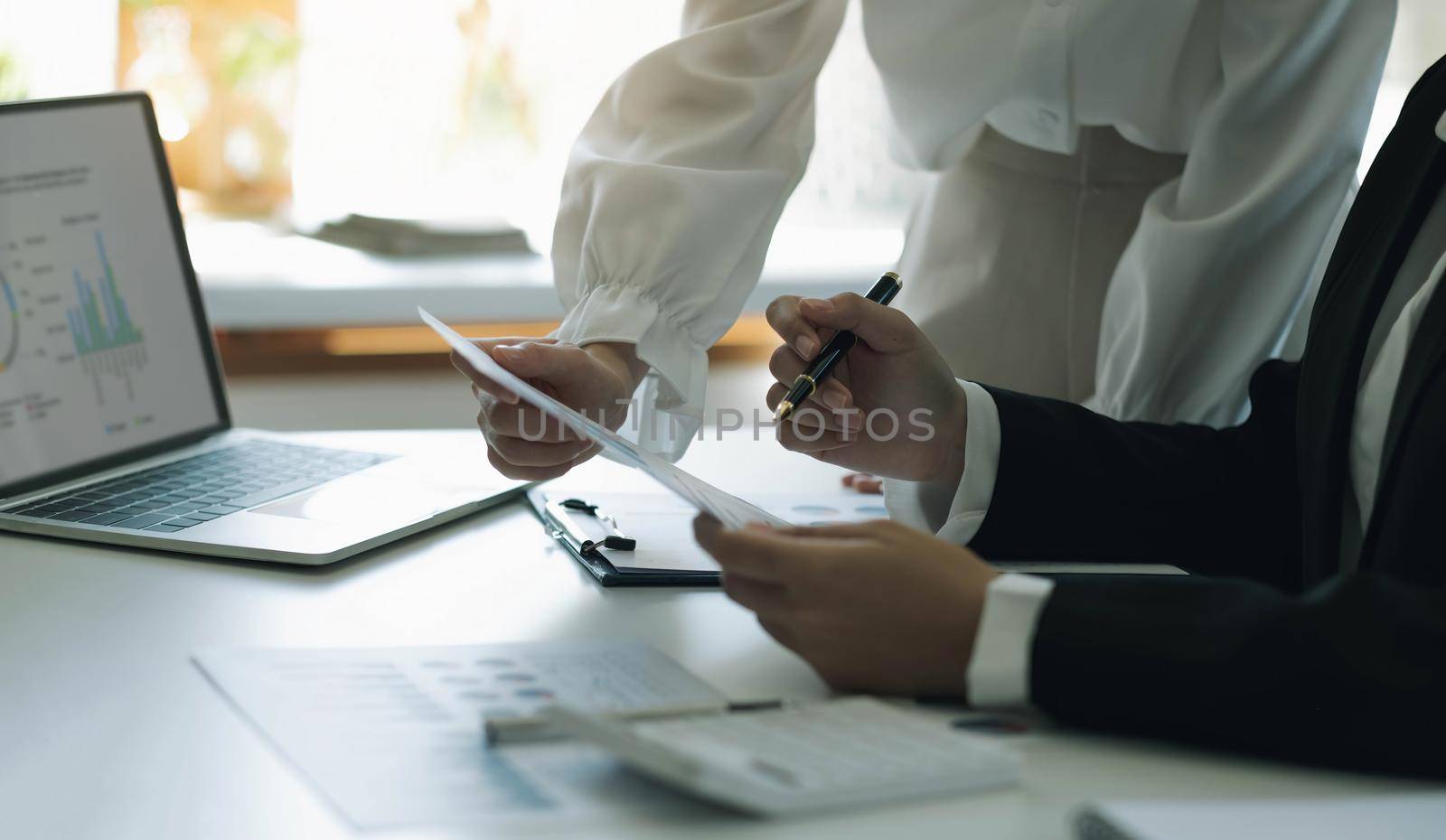 Close up team businesswoman studying statistics and holding a graph document by hand An office worker stood near the desk with a laptop. woman pointing finger