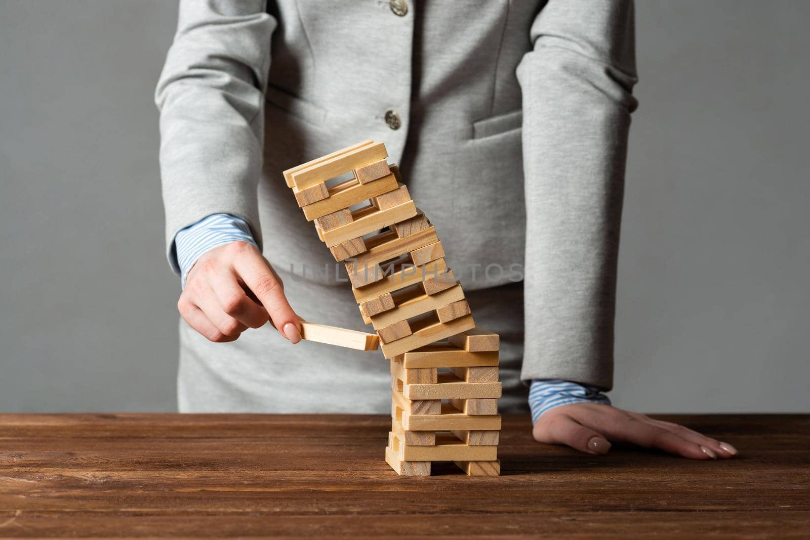 Businesswoman removing wooden block from falling tower on table. Management of risks and economic instability concept with wooden jenga game. Failure and collapse in corporate business