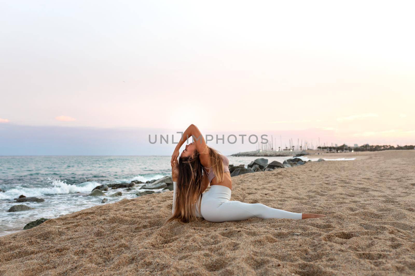 Flexible young caucasian woman practicing the splits yoga pose on the beach at sunset. Copy space. by Hoverstock