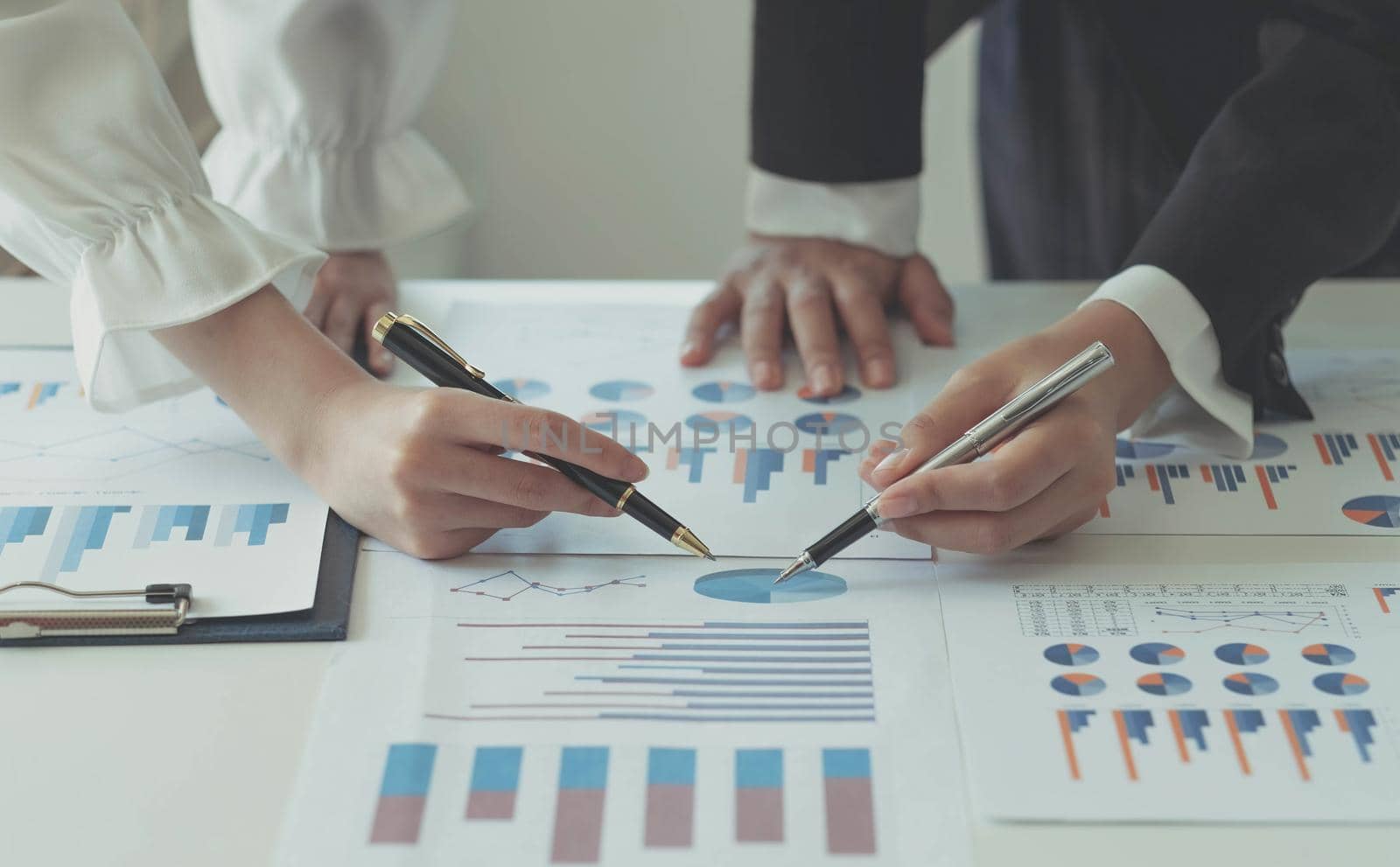 Close-up of two women's hands pointing to a turnover chart while talking on a wooden table in the office. group support concept by wichayada