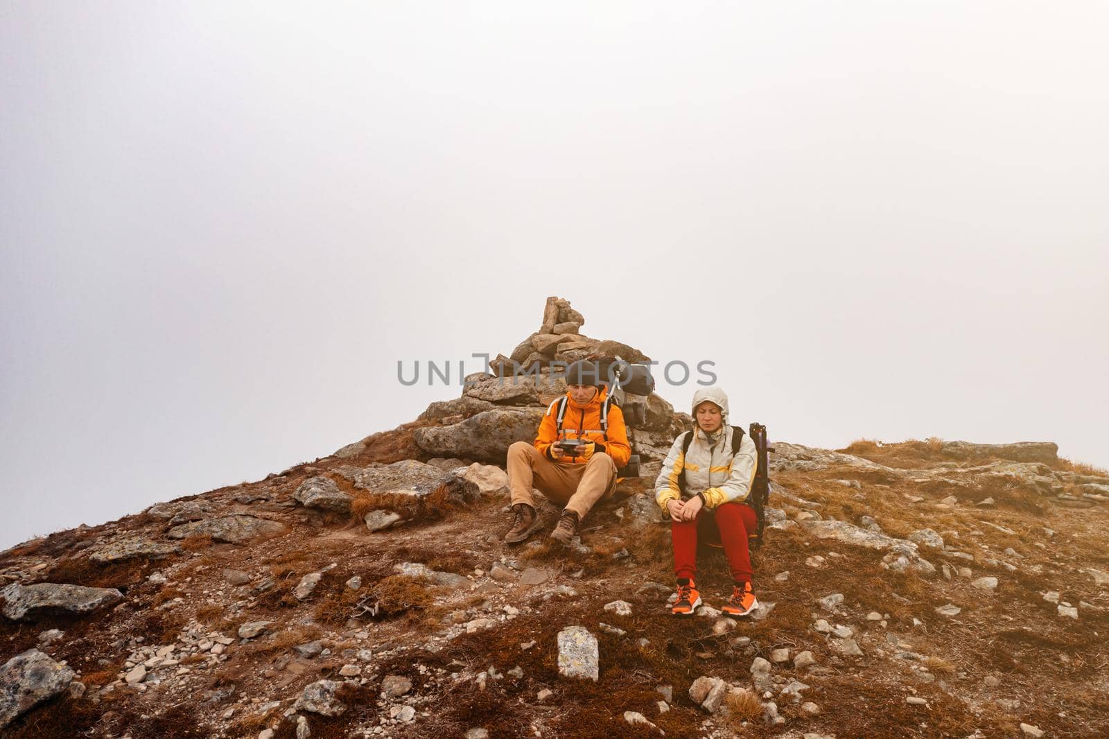 Tourists walk through the Ukrainian Carpathians, tourists carry heavy backpacks on their backs, two tourists sit on top of Mount Spitz.