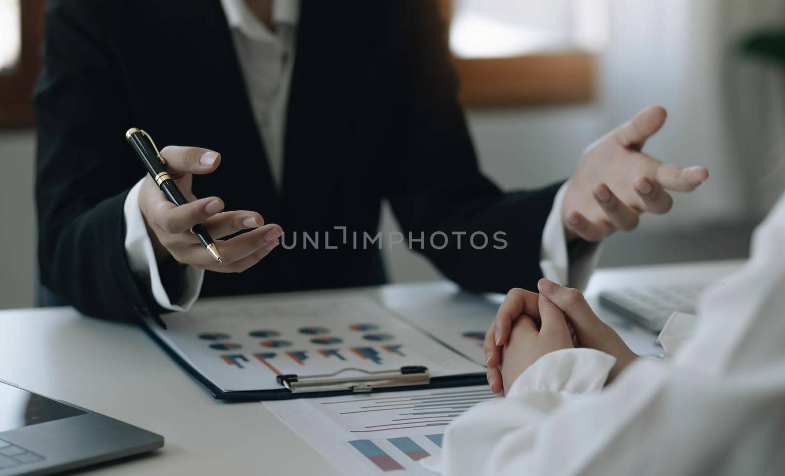 Team businesswoman explaining the structure of the business and another employee listens discreetly. along with the documents on the desk and laptop in the office by wichayada