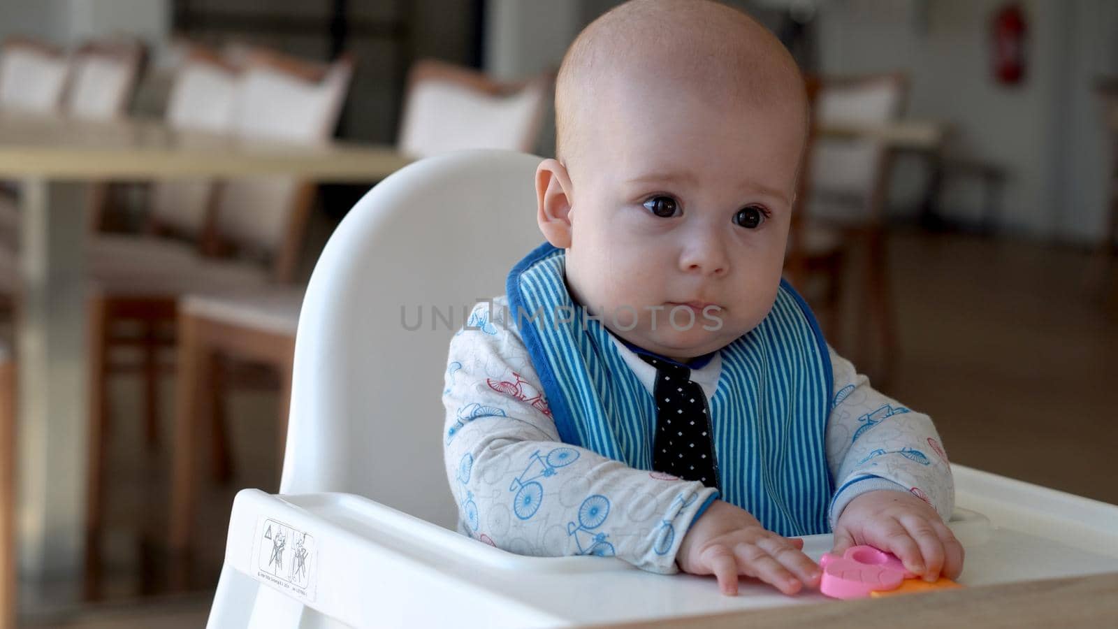 mom Mother feed young baby in white feeding up high chair, first supplement vegetable puree Happy smiling kid eat for the frst time, child with dirty face, little infant boy eating porridge nutrition.