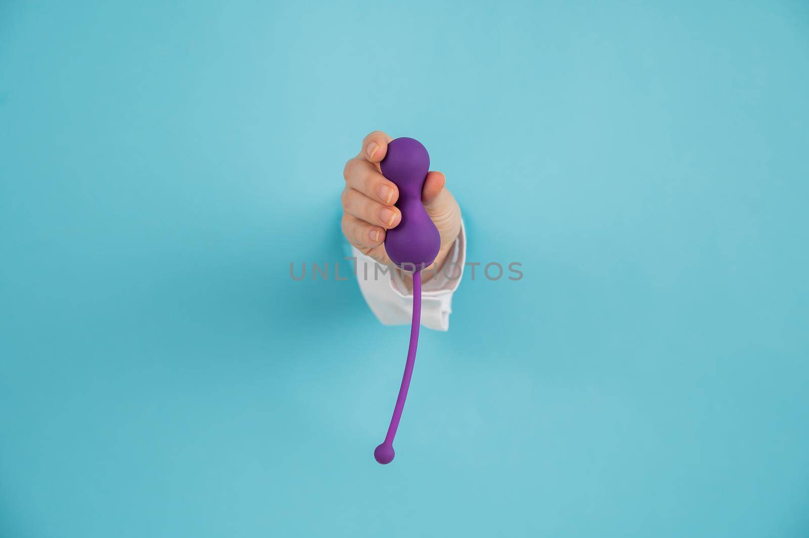 Female hand sticking out of a hole in a blue background and holding a kegel machine