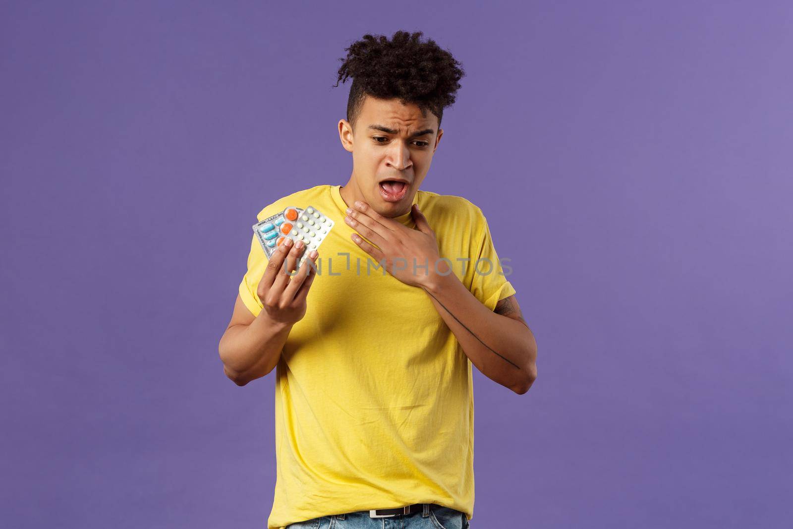 Health, influenza, covid-19 concept. Portrait of young man coughing, choking with tablet, drank pill without water, holding drugs and touch neck as suffer sore throat, purple background.