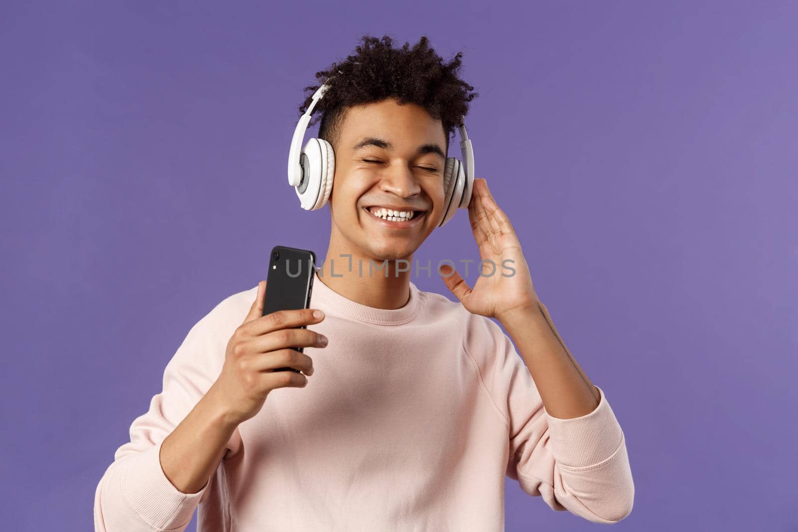 Technology and lifestyle concept. Portrait of carefree attractive young man enjoying fine sound, listening music with headphones look delighted awesome quality of bass, hold mobile phone by Benzoix