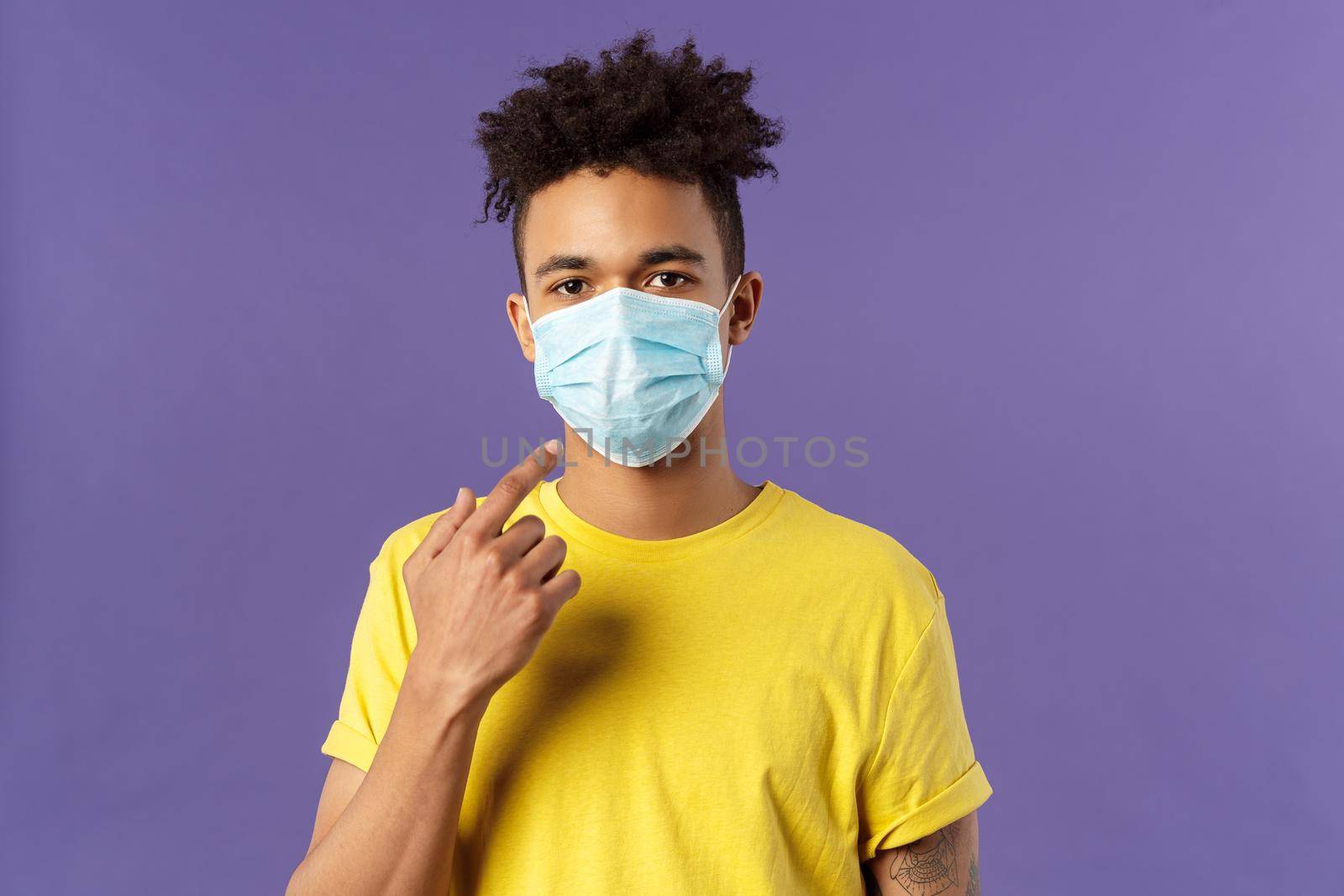 Covid19, healthcare and medicine concept. Young hispanic guy with afro haircut, wear and point at face mask, social-distancing during pandemic, explain friends how to prevent catching disease.