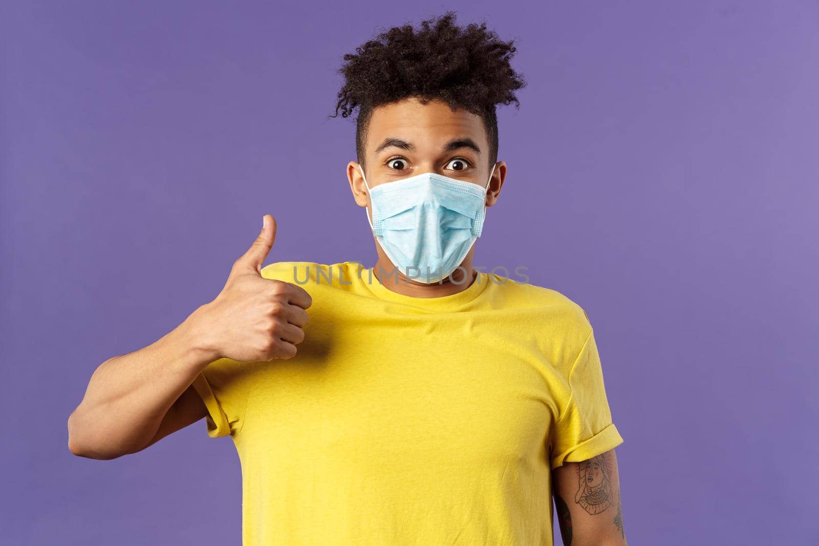 Covid19, healtcare and medicine concept. Excited young hispanic man in facial mask taking care of health, avoid public places, stay home and encourage be safe indoors, show thumbs-up, smiling.