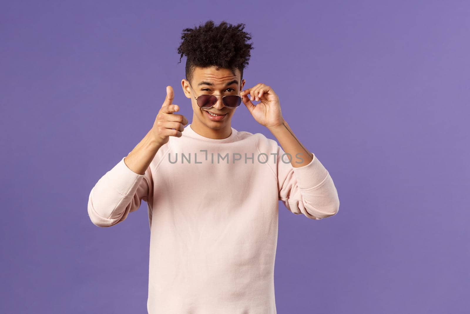 Portrait of cheeky handsome young man wearing sunglasses, take them off and show thumb-up, like or approval, recommendation sign, smirk satisfied, saying all good, alright, purple background by Benzoix
