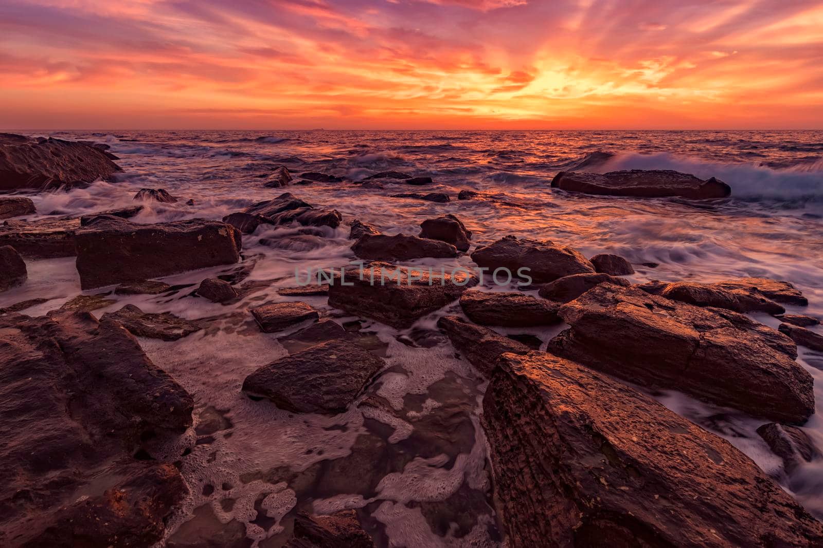 Rocks on the stone beach at sunset. Twilight sea and sky. Dramatic sky and clouds. Nature landscape.
