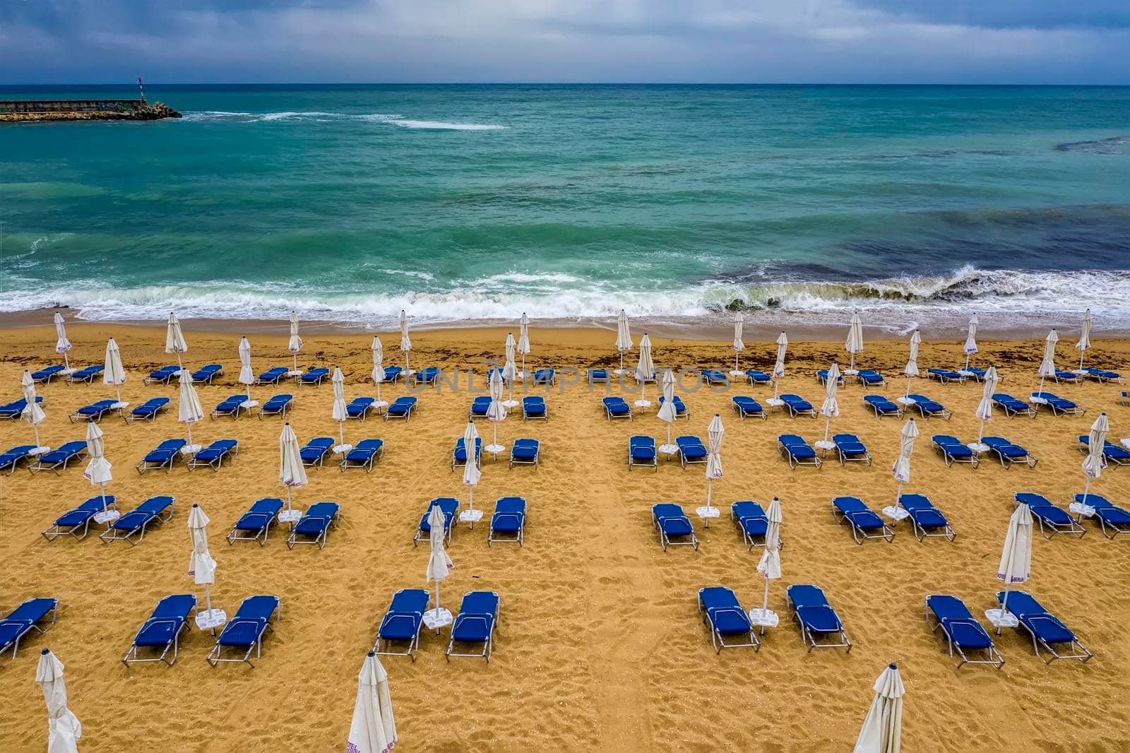 Aerial view of an amazing beach with, blue lounge chairs, with umbrellas, and turquoise sea.