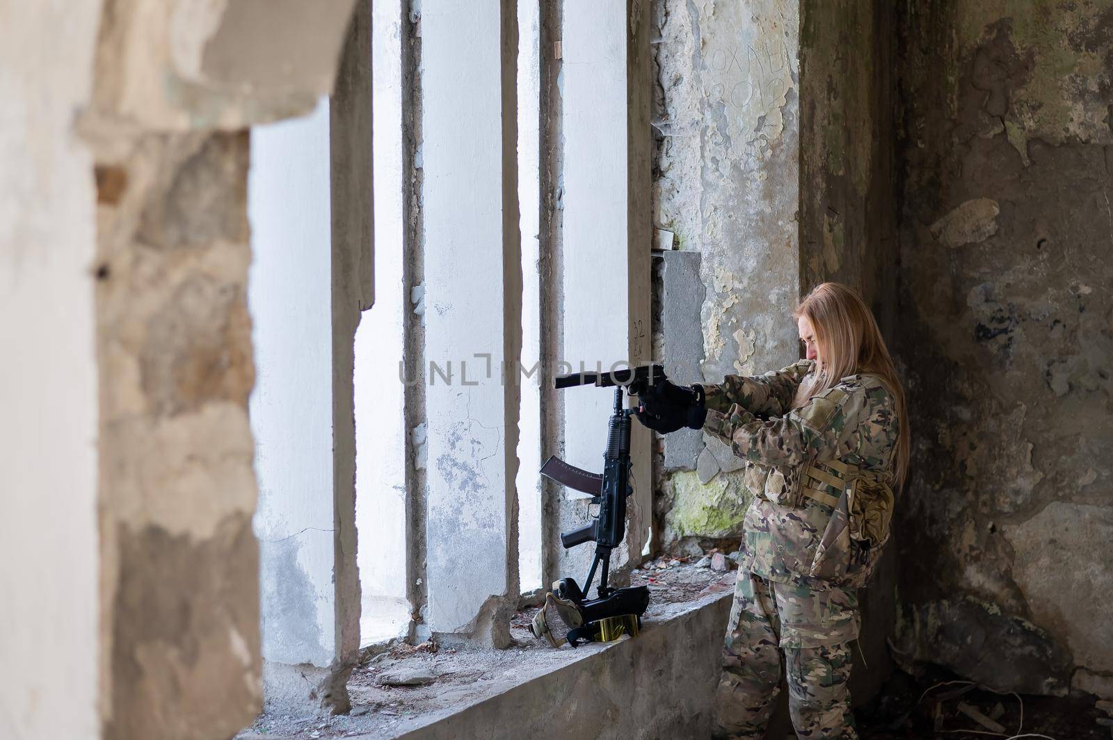 A woman in an army uniform aims to shoot a firearm in an abandoned building