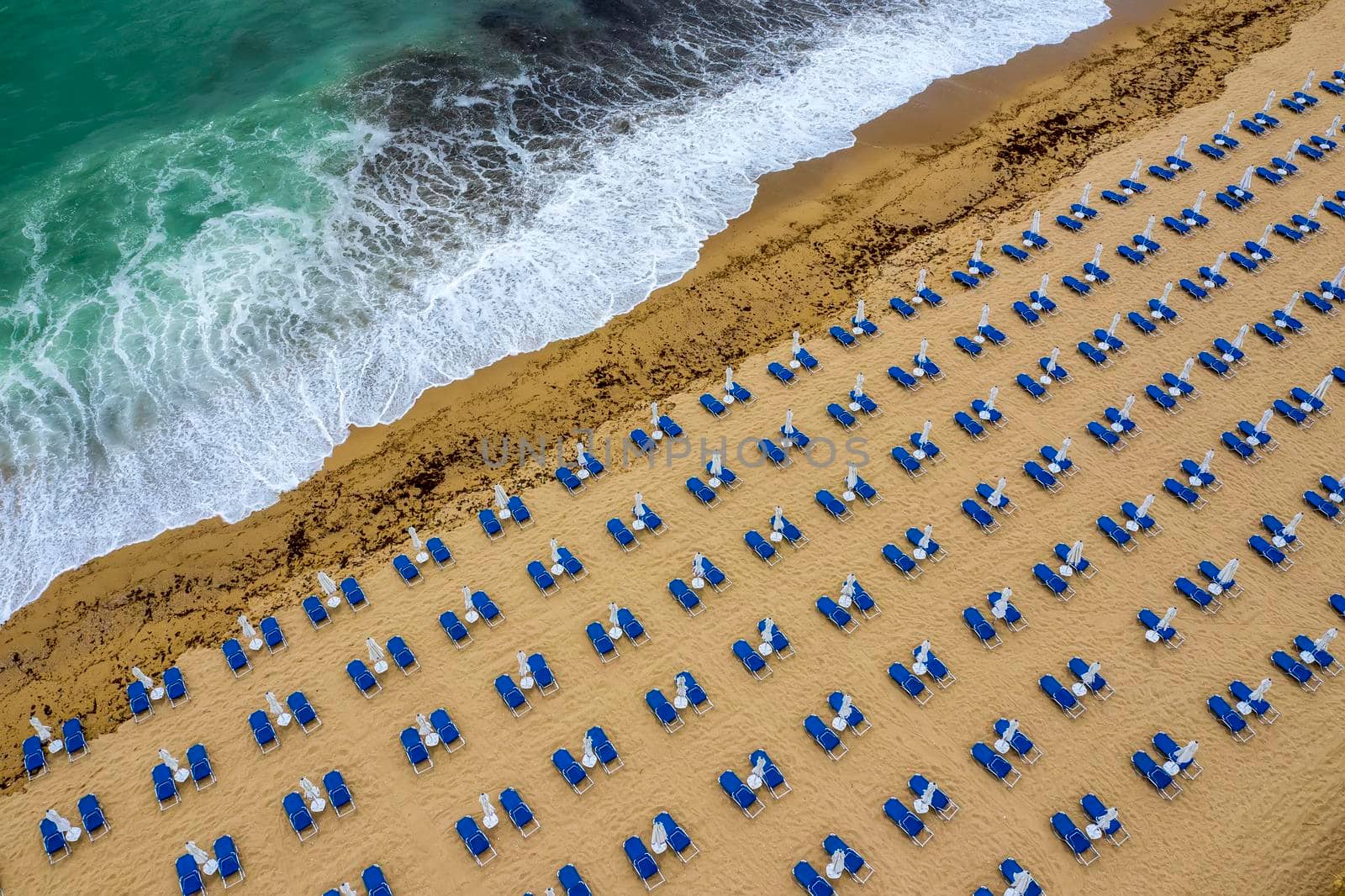 Aerial view of an amazing beach with white umbrellas, lounge chair, and turquoise sea.