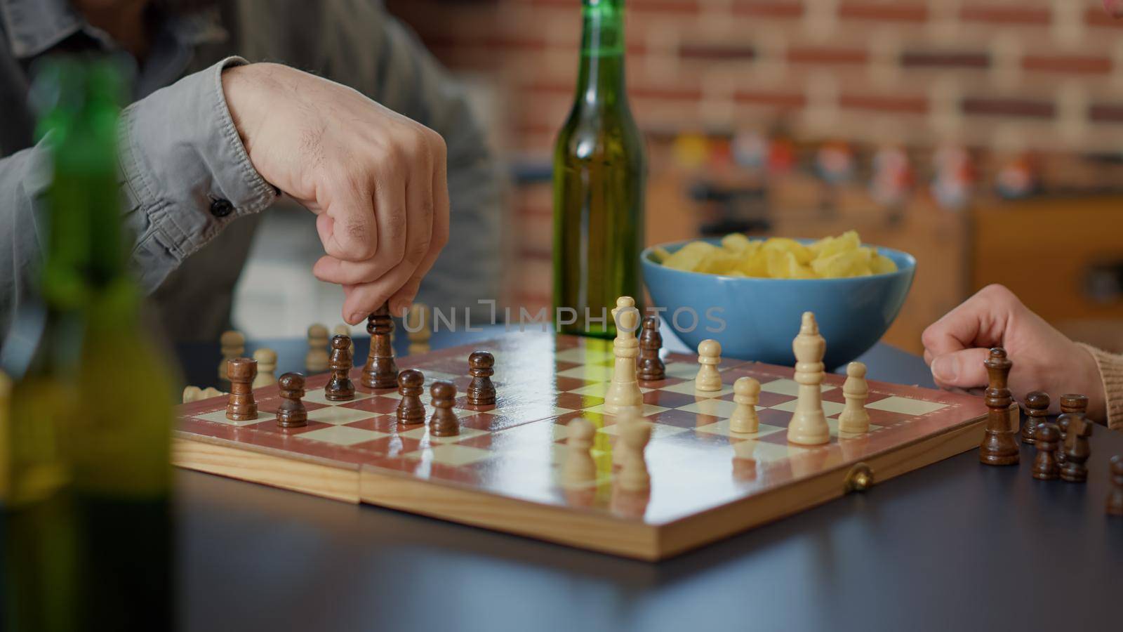 Young people having fun with chess board games play, serving alcoholic drinks and snacks. Group of friends playing match on table for entertainment at gathering. Tripod shot. Close up.