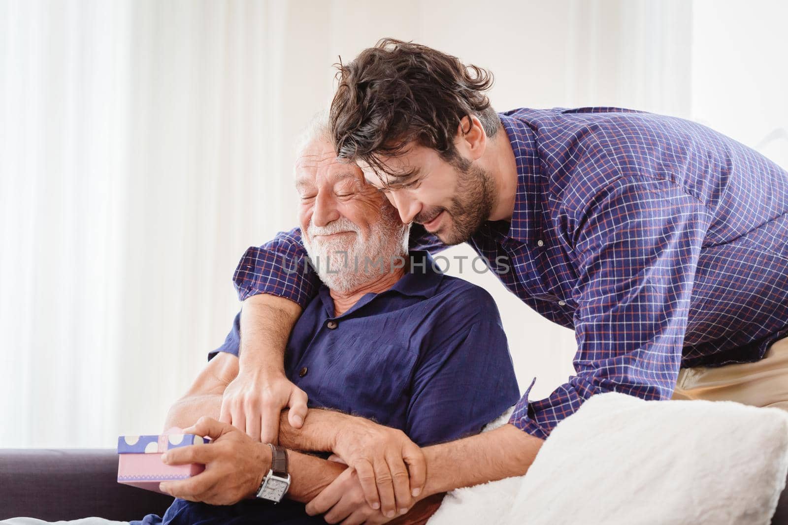 young man hugs the uncle old man warmly inside the house, son happy and love his father or grand father with gift box concept by qualitystocks