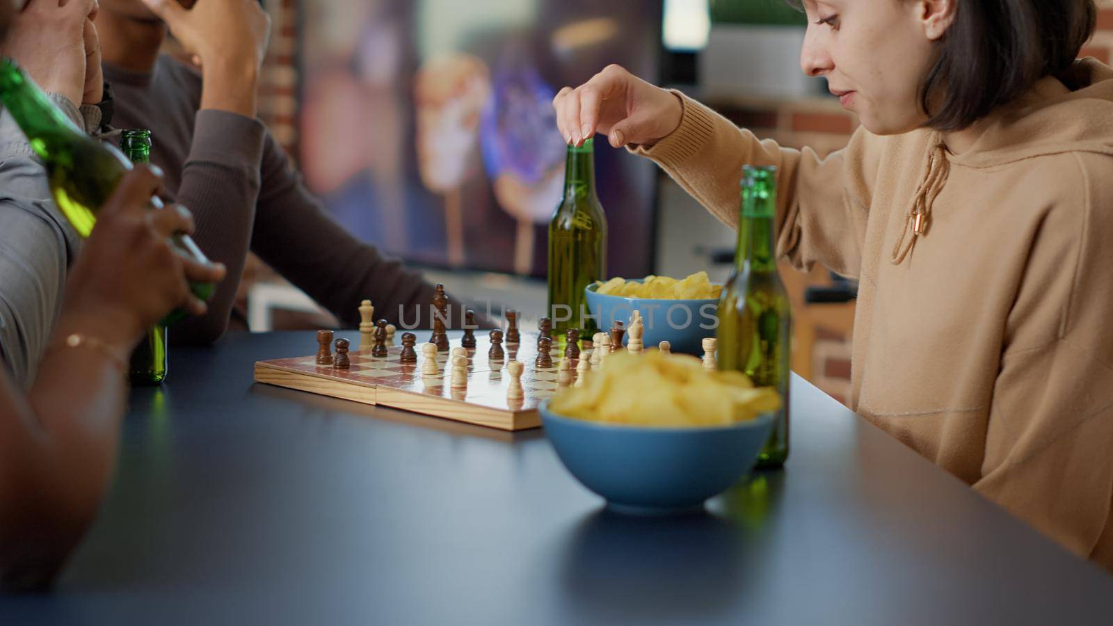 Focused woman playing strategic board games with friends, having fun with chess match and competition at home. Happy people enjoying gameplay together, serving beer. Handheld shot. Close up.