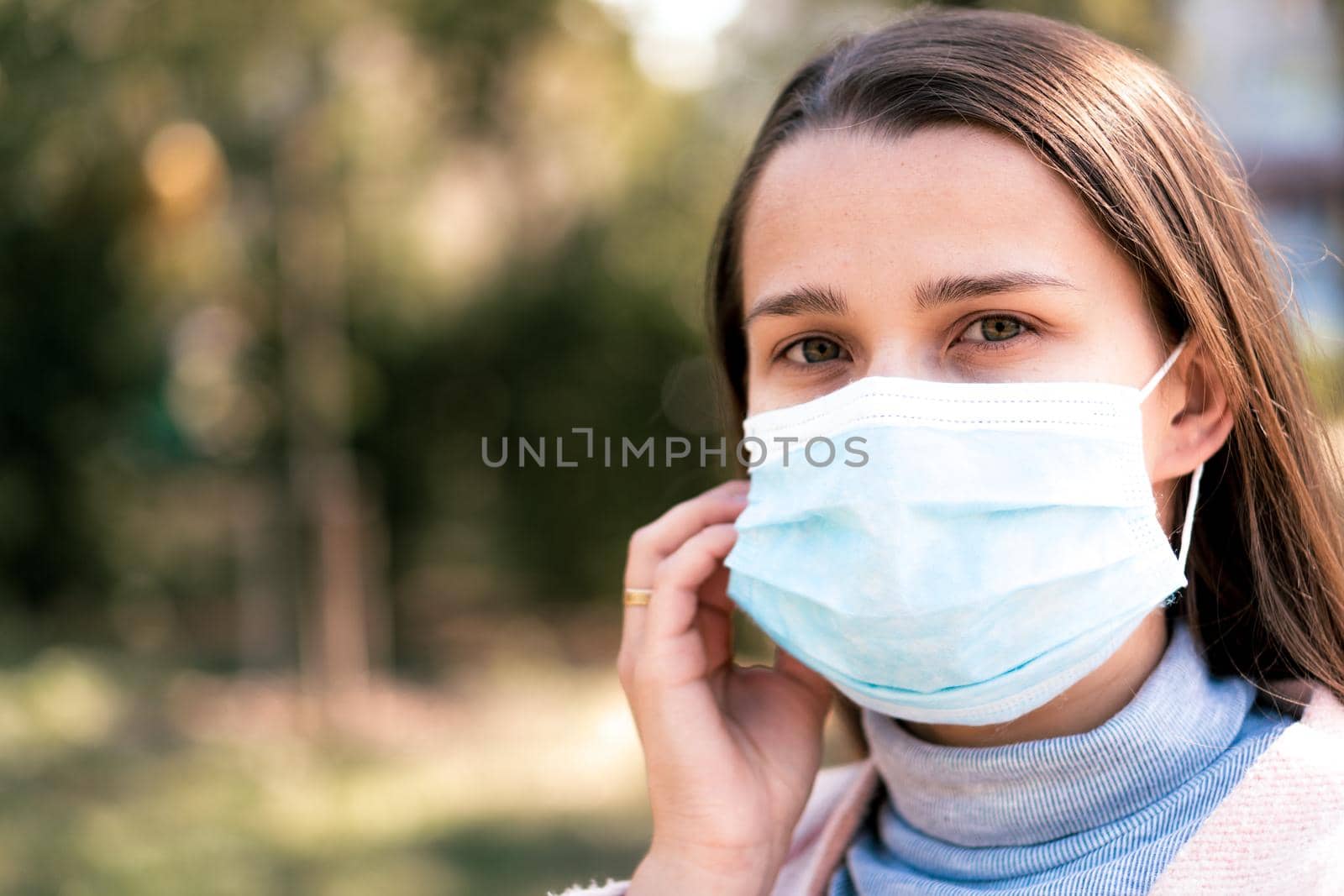 care, infants, spring, coronavirus and quarantine concept - Young cute long haired woman European Caucasian Slavic appearance put on blue medical protective mask in midday sunlight backlight in park