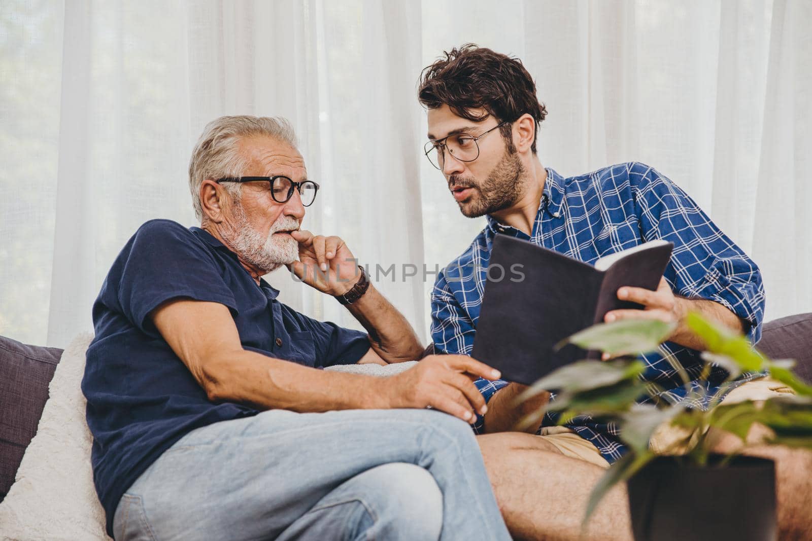 Young man consulting business project or education lecture content in text book with retired senior elder at home