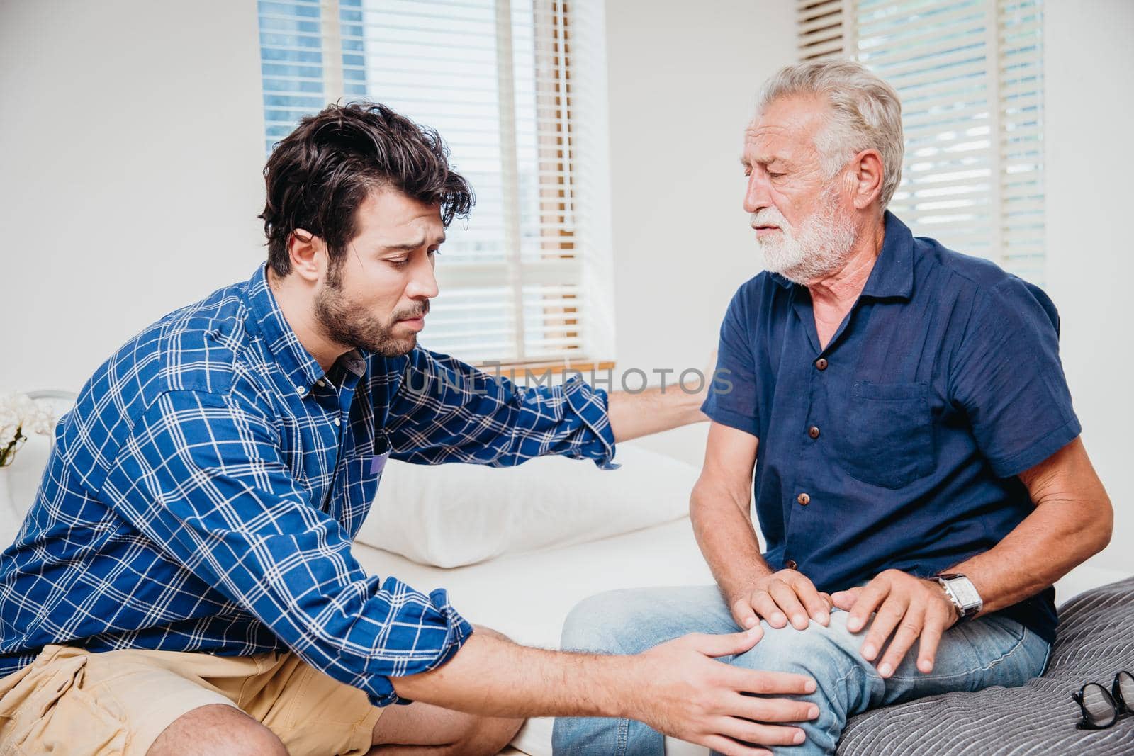 Young men health care elderly uncle in the home, old man pain at knee leg. by qualitystocks