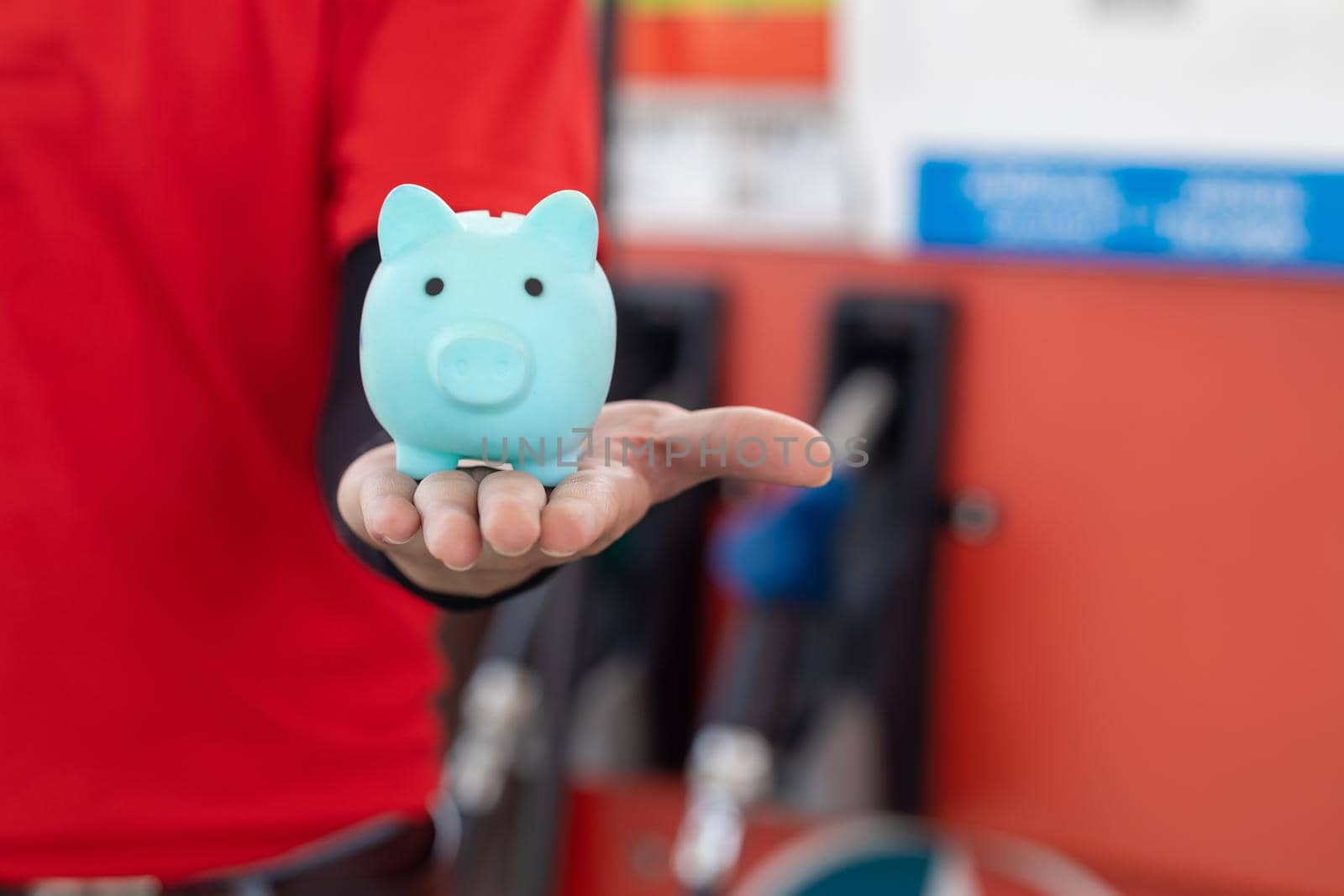Gas station staff worker with piggy bank for save money from low fuel price, gas costs reduction, cut and saving gasoline drop price concept. by qualitystocks