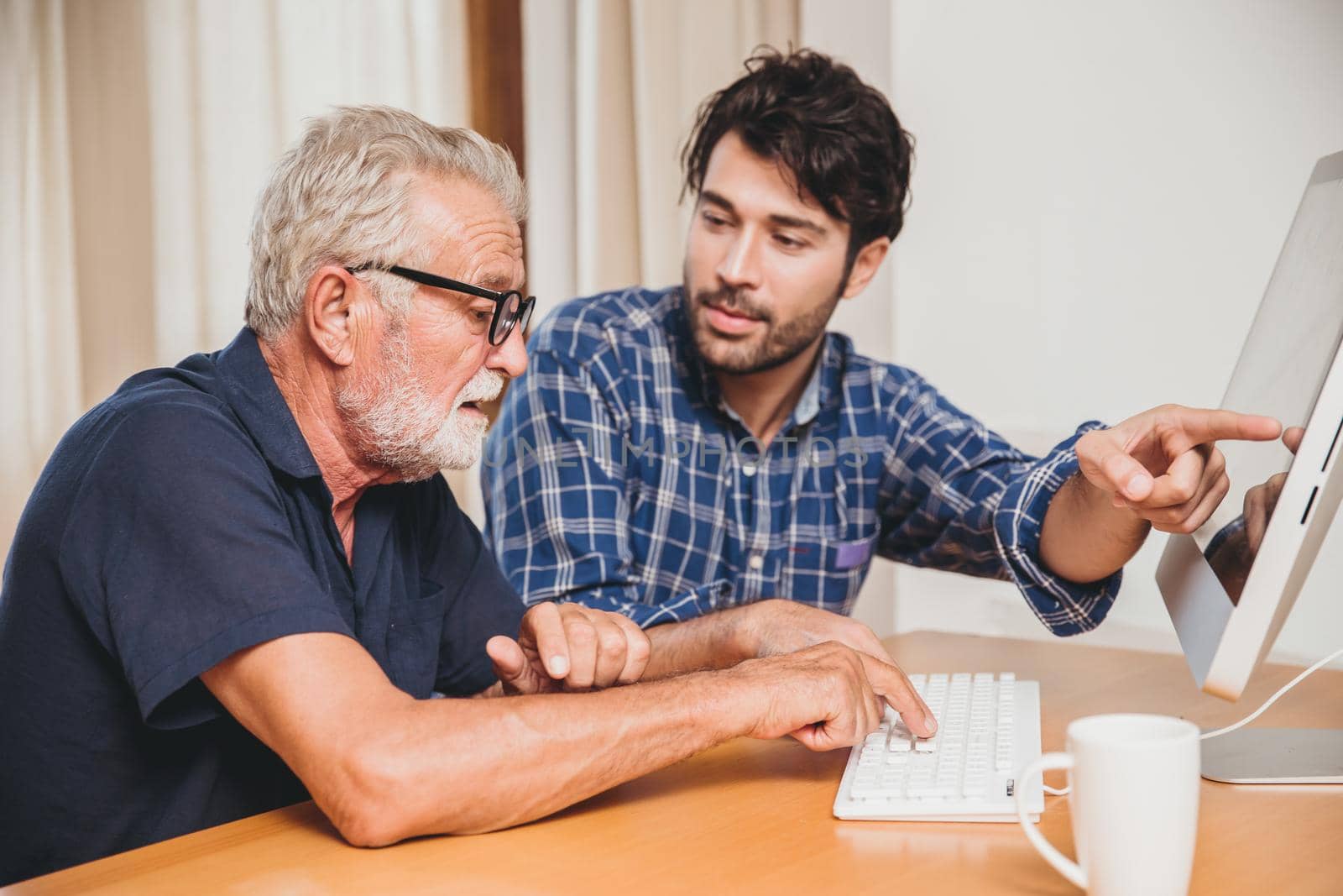 young man or son teaching his grandfather elderly dad learning to using computer at home. by qualitystocks