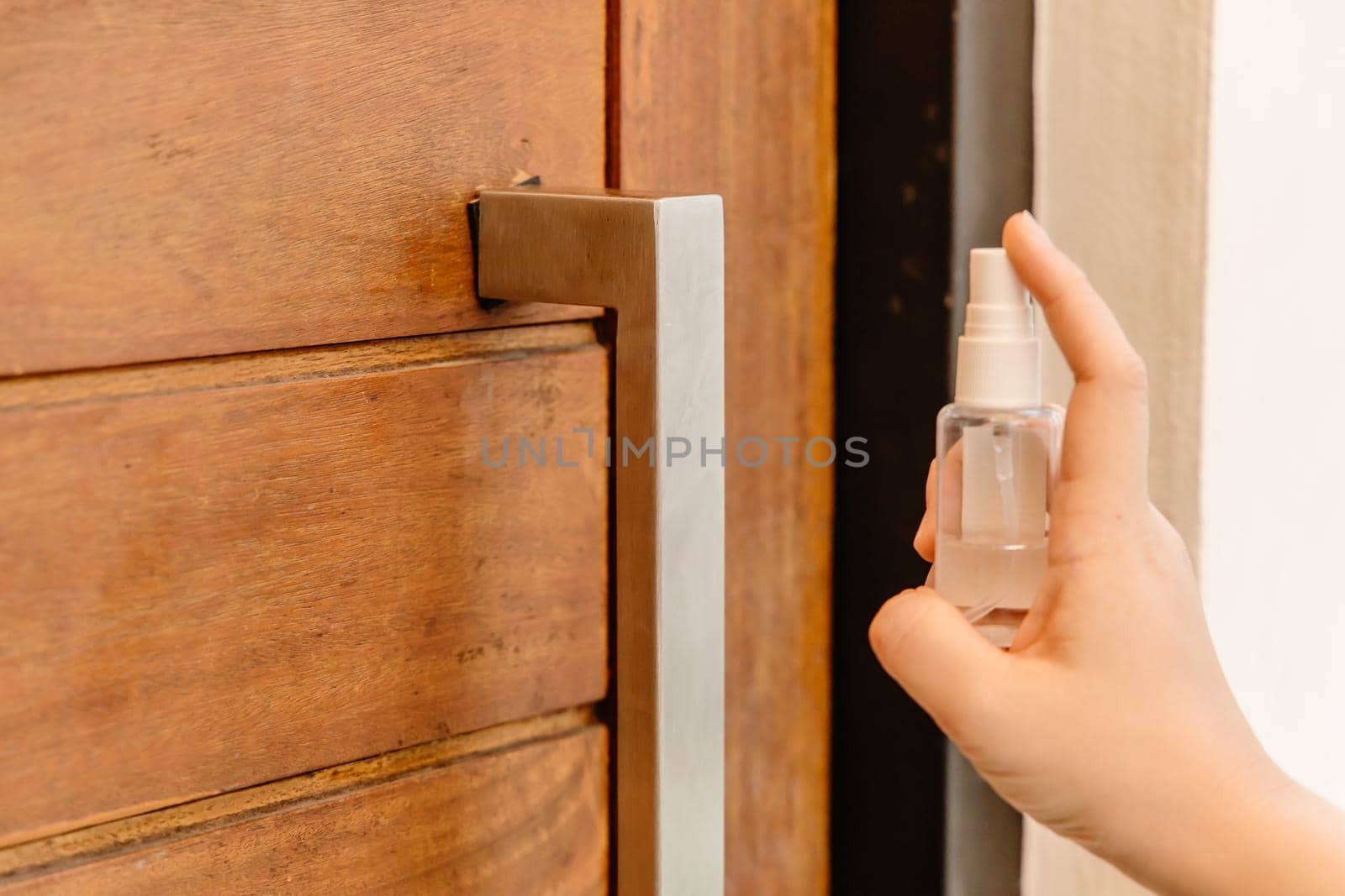 Closeup people using alcohol disinfectant spray cleaning door handle for preventing spreading of virus or germ when touching.