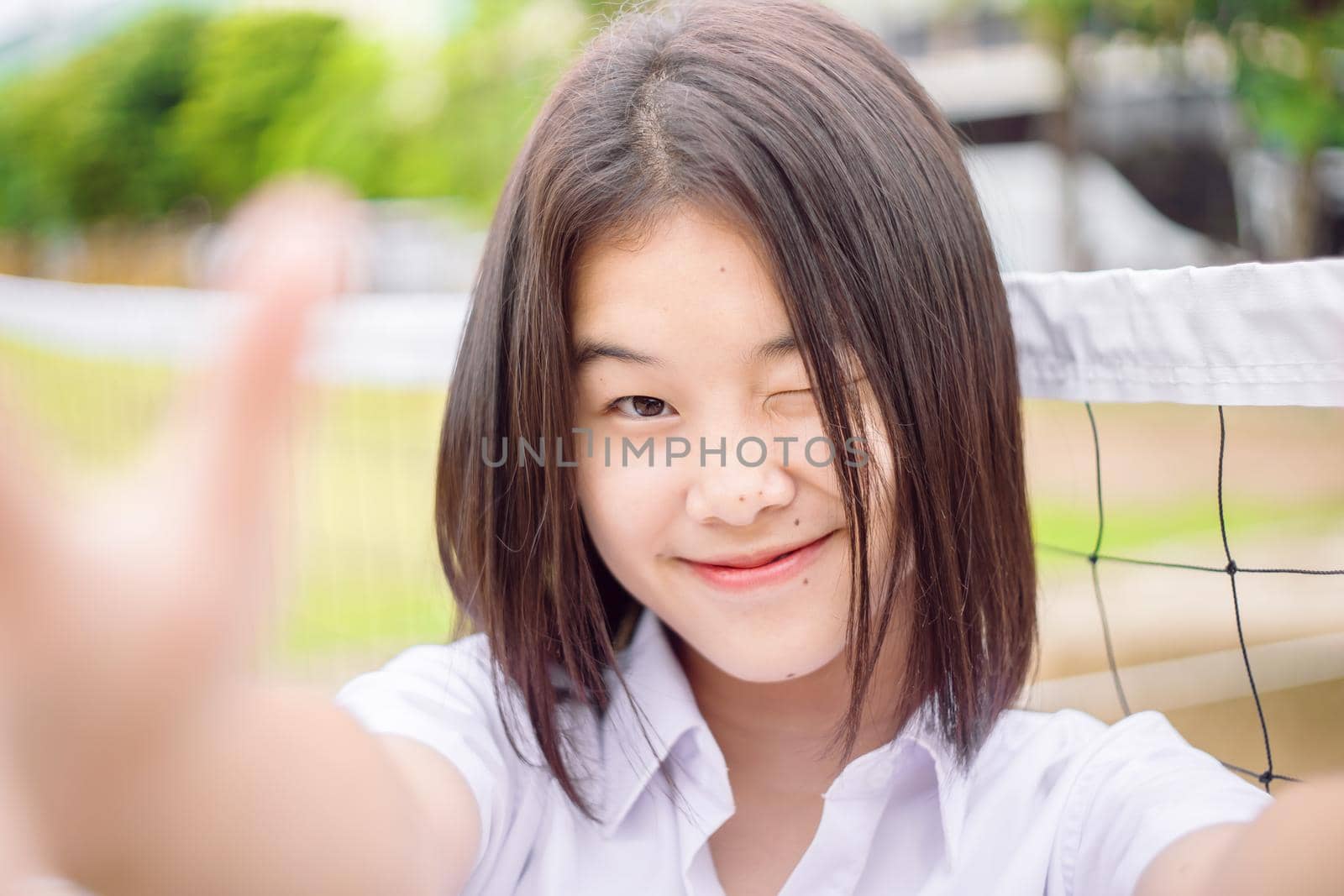 Cute asian student girl winking eye smiling expression selfie camera, close-up shot by qualitystocks