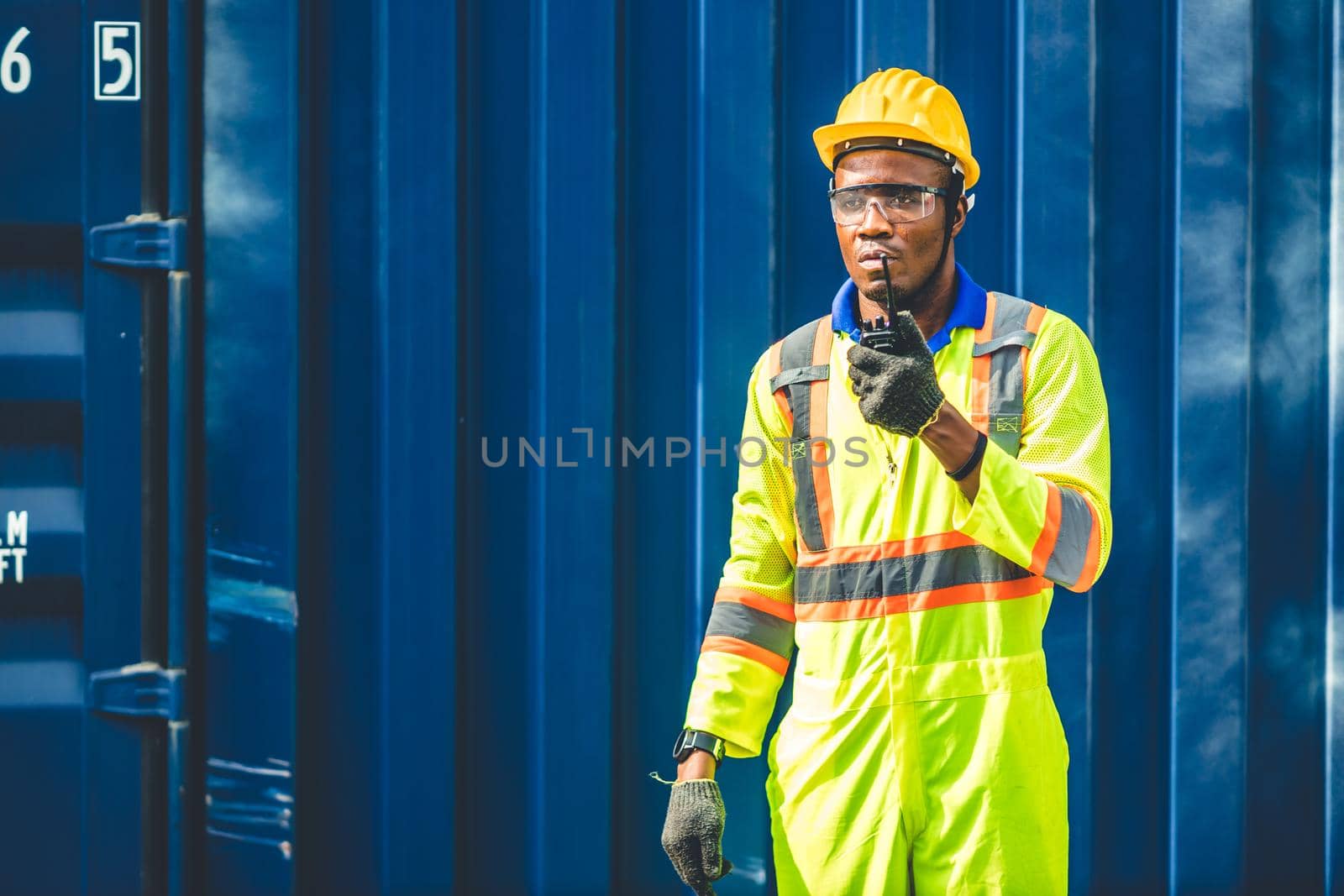 Black African worker working in logistic shipping radio control order command loading containers at shipping port. staff cargo for import export goods logistic. by qualitystocks