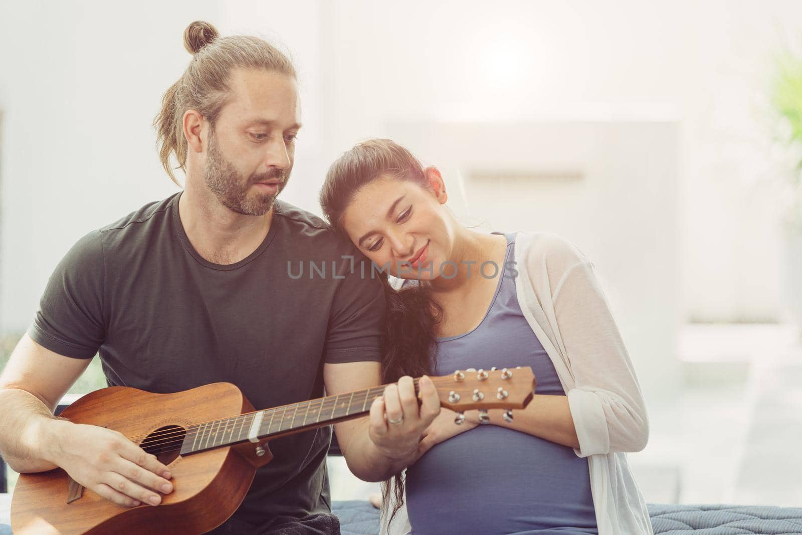 Husband with pregnant wife stay home lovely playing guitar music for baby kissing and showing love together