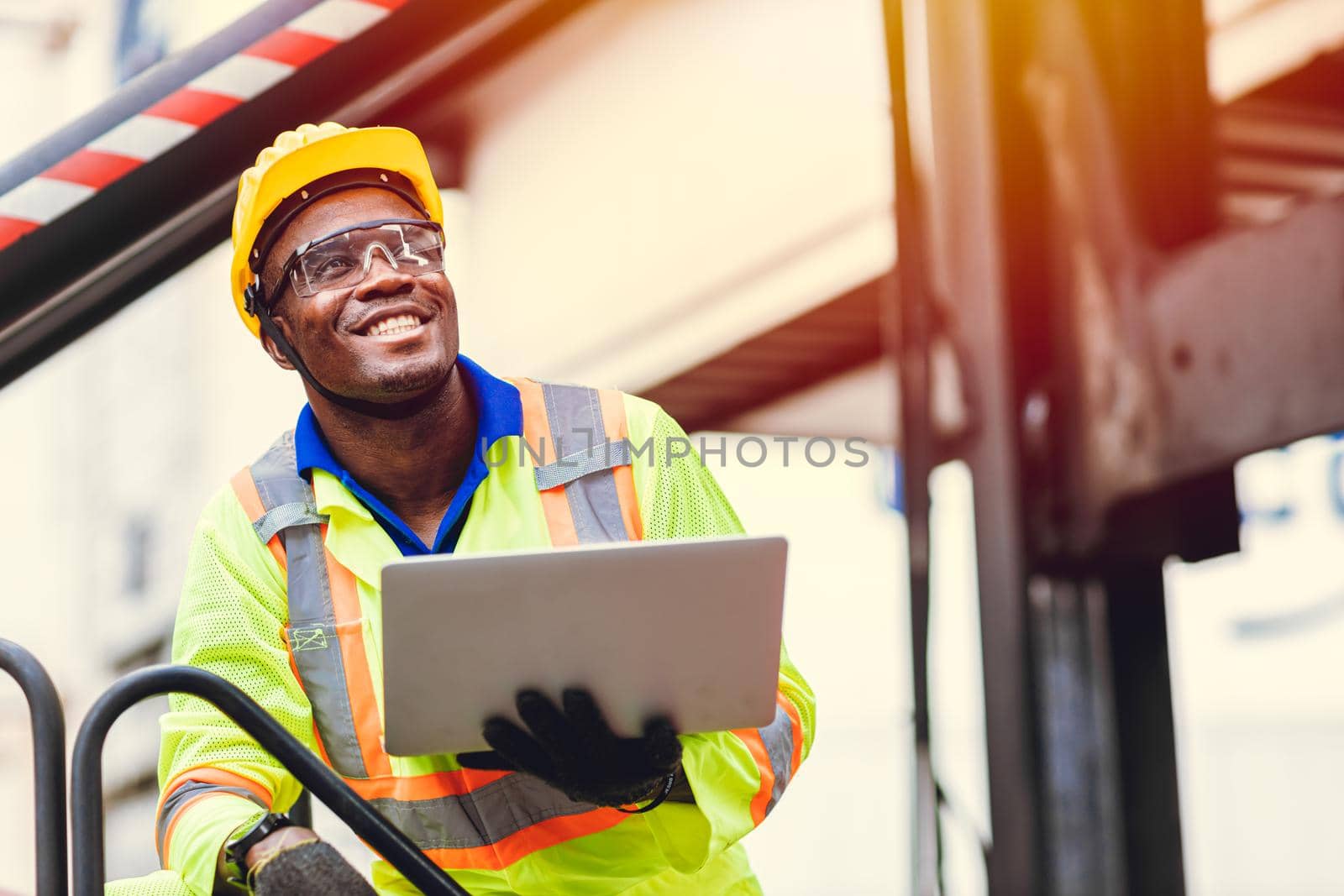 Black African happy worker working in logistic shipping with laptop computer control loading containers at port cargo. Import export shipping industry people. by qualitystocks