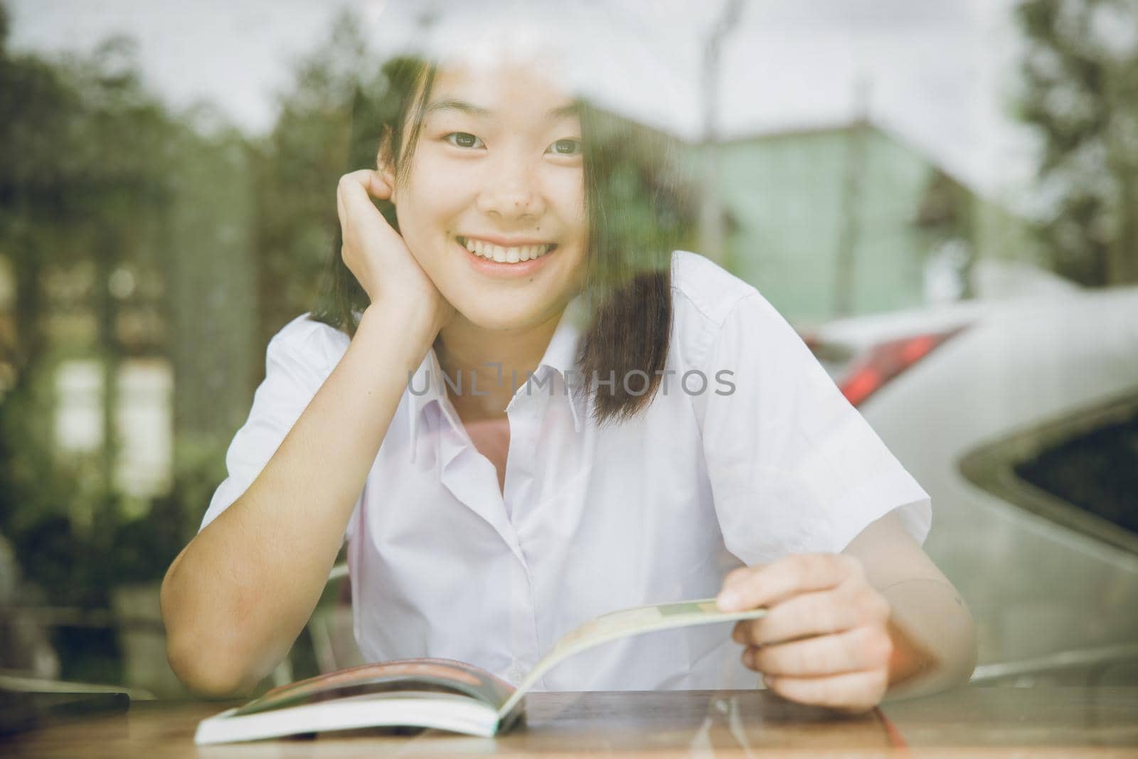 Asian university girl teen cute smiling looking through glass window shadow reflect effect while sitting reading book