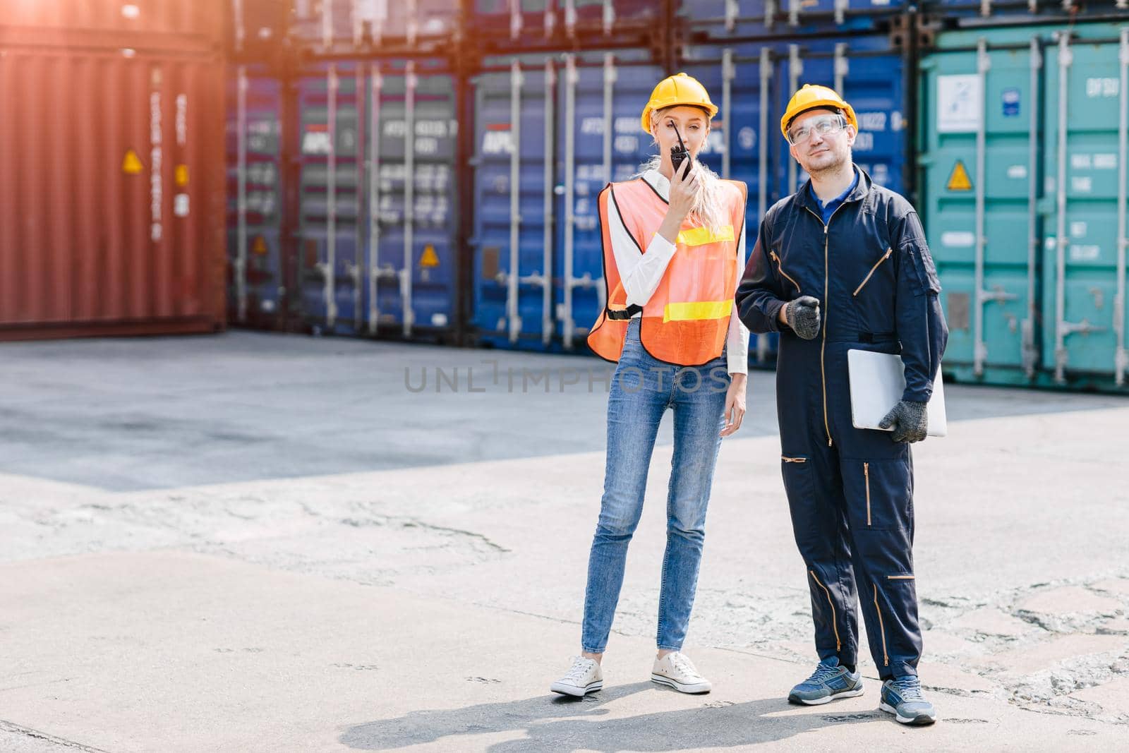 logistic worker man and woman working team with radio control loading containers at port cargo to trucks for export and import goods. by qualitystocks