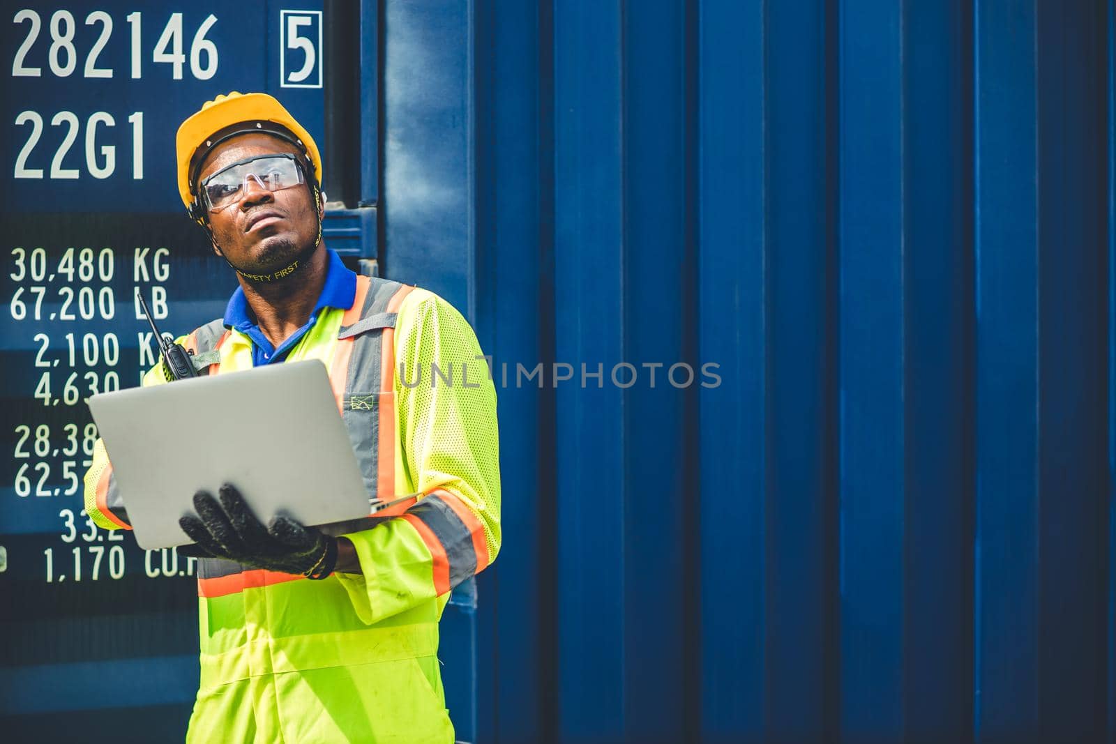 Black African worker working in logistic shipping using laptop to control loading containers at port cargo for import export goods foreman looking high for future