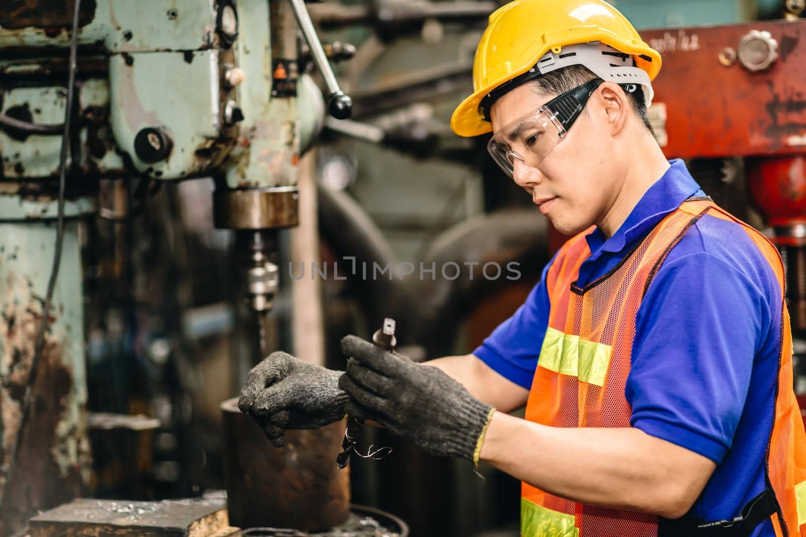 Engineer worker checking and replace a drill bit of metal drilling machine in heavy industry factory.