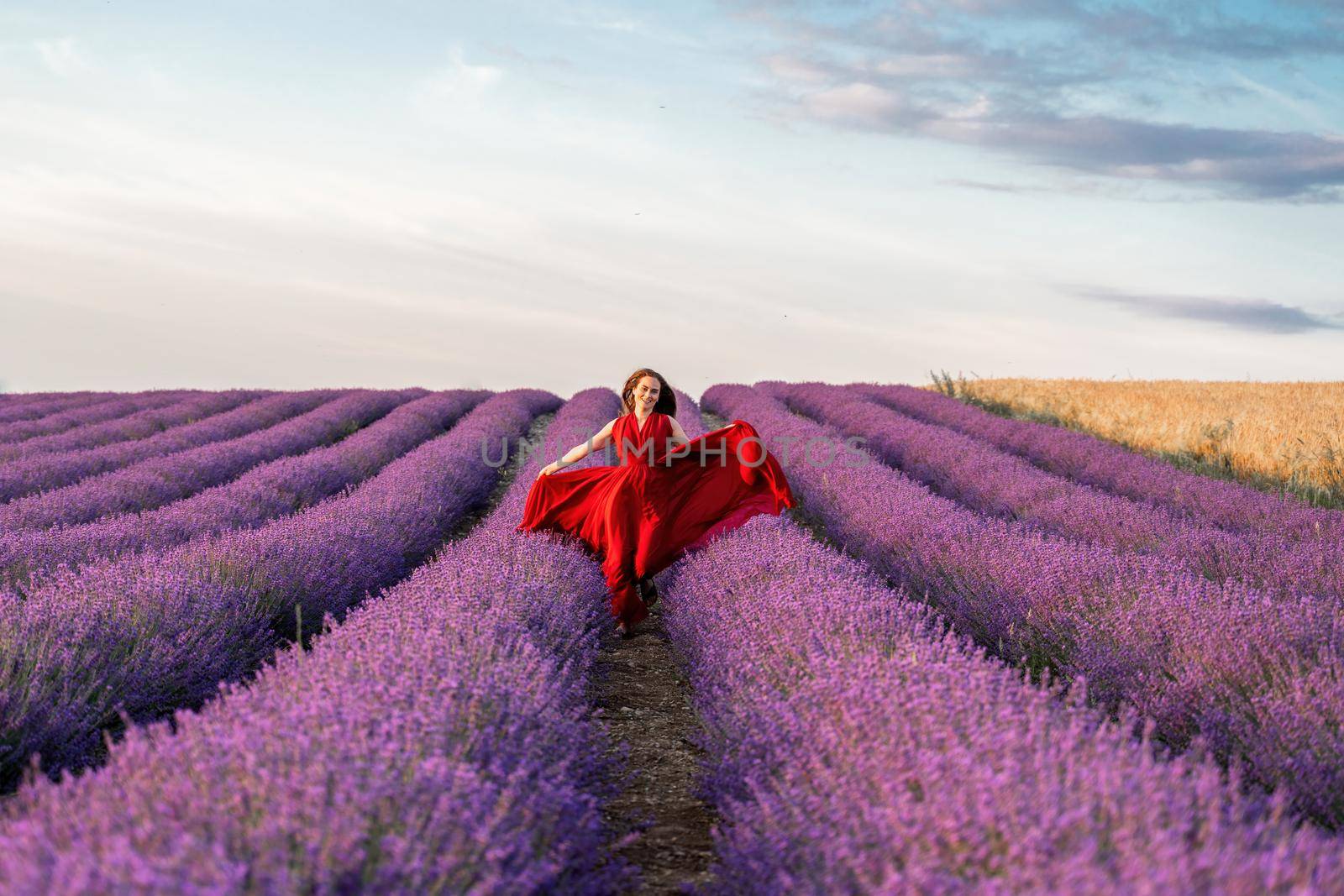 Among the lavender fields. A beautiful girl in a red dress runs against the background of a large lavender field.