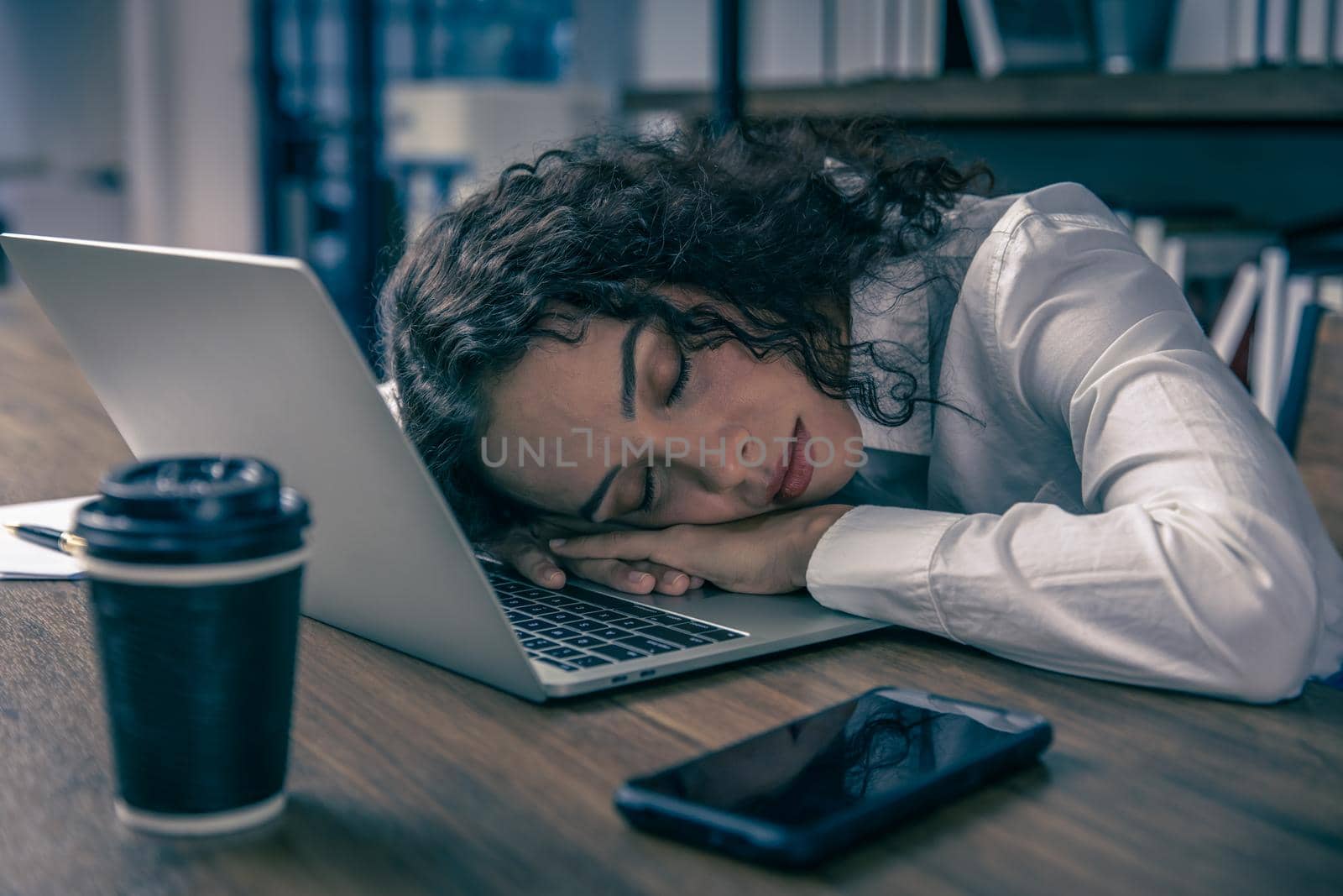 Tired working women sleeping at office desk hard work overnight nap. African American black businesswomen employee worked late and fell asleep on the computer laptop table at night with coffee cup.