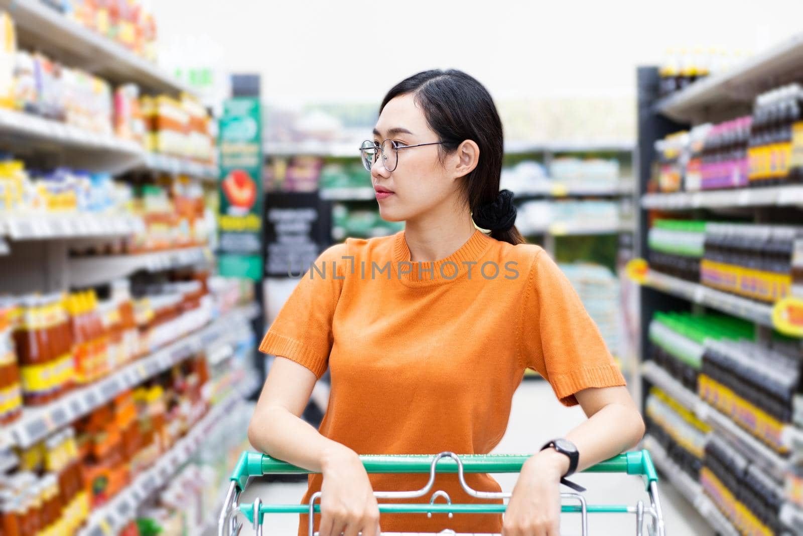Asian woman enjoying shopping in shopping mall handle shopping cart looking at supermarket shelf