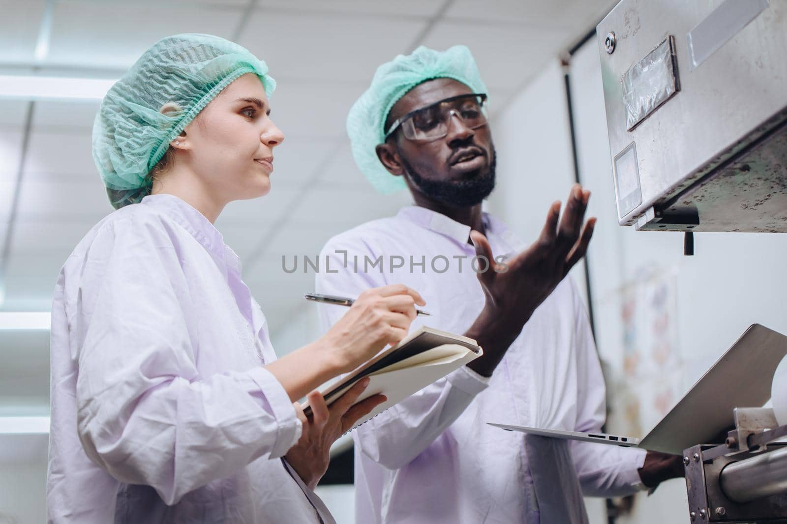 Woman production supervisor working with African worker in food factory to checking and report machine problem to engineer in production line. by qualitystocks