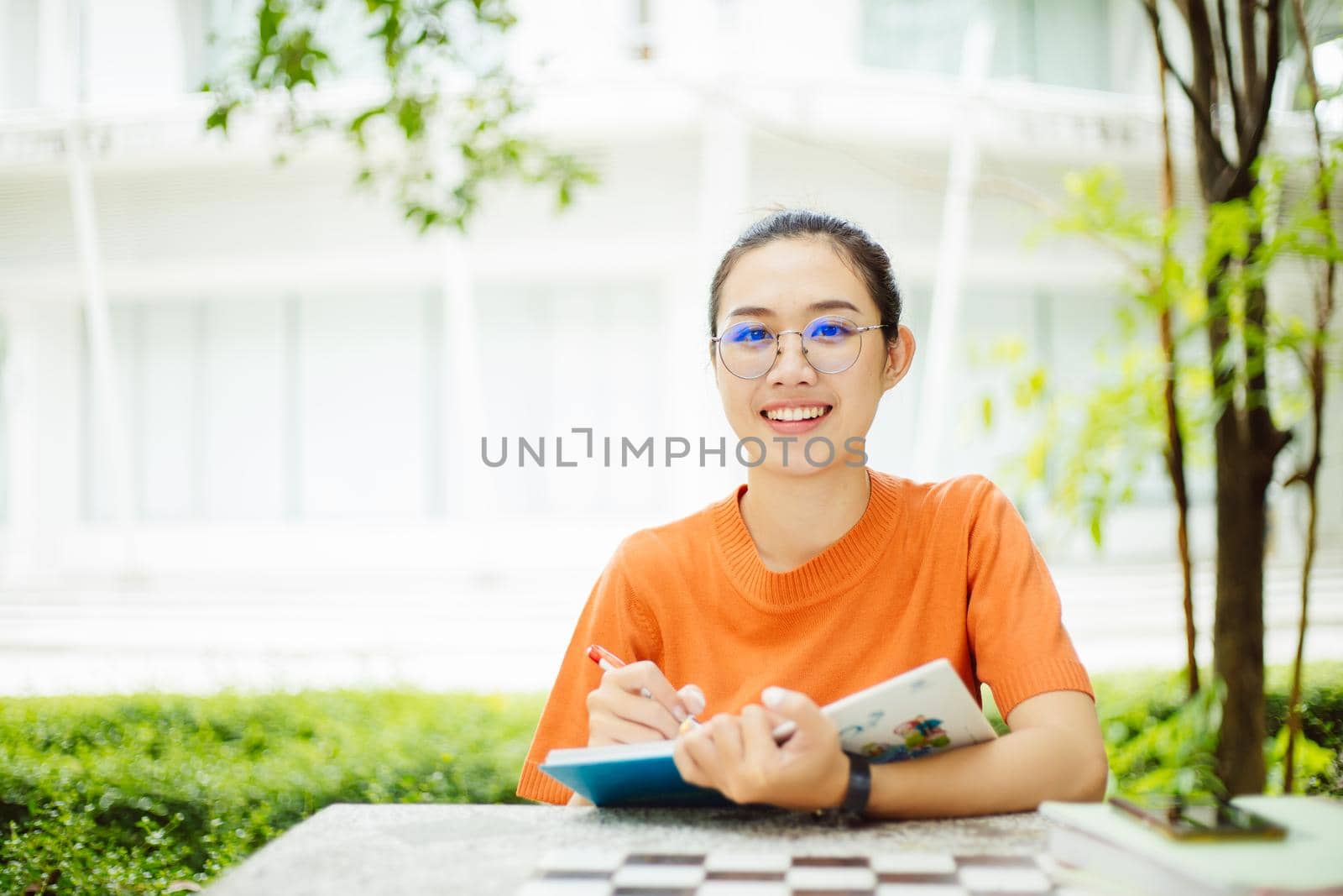 Portrait of nerd Asian woman girl smart teen happy smiling with glasses at green park outdoor in university campus with copyspace