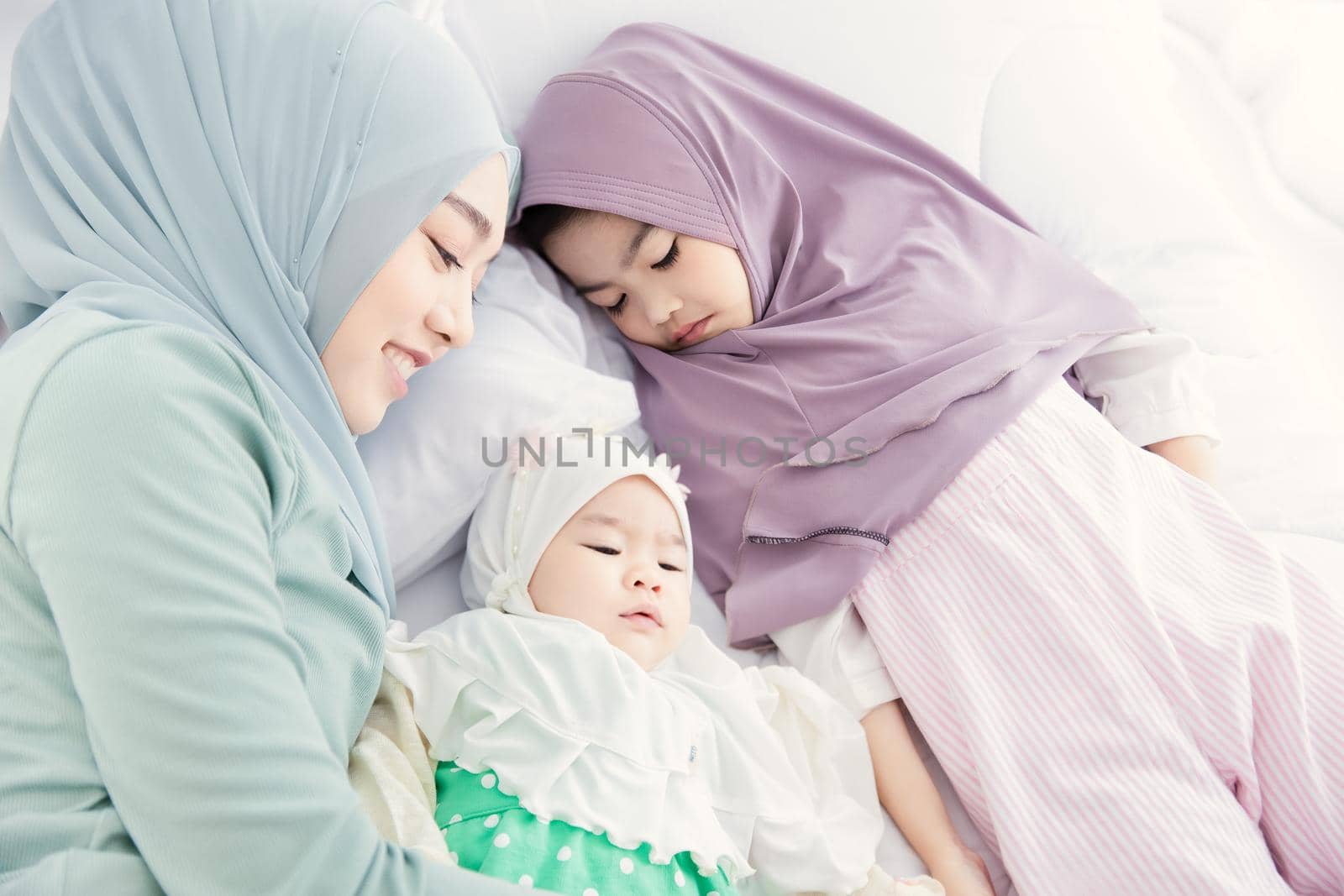 Muslim Hijab mother keep looking and cuddling sleeping baby with love and care on the bed.