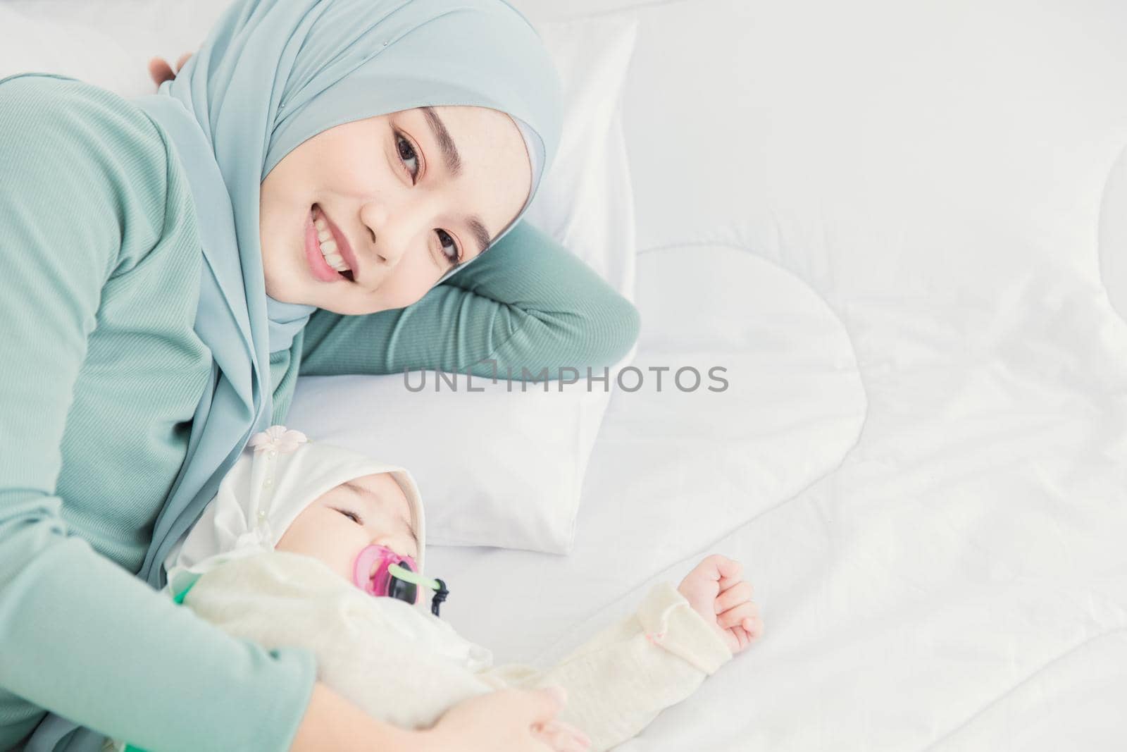 Muslim Hijab stay with her baby on white bed smiling at home, mother care infant.