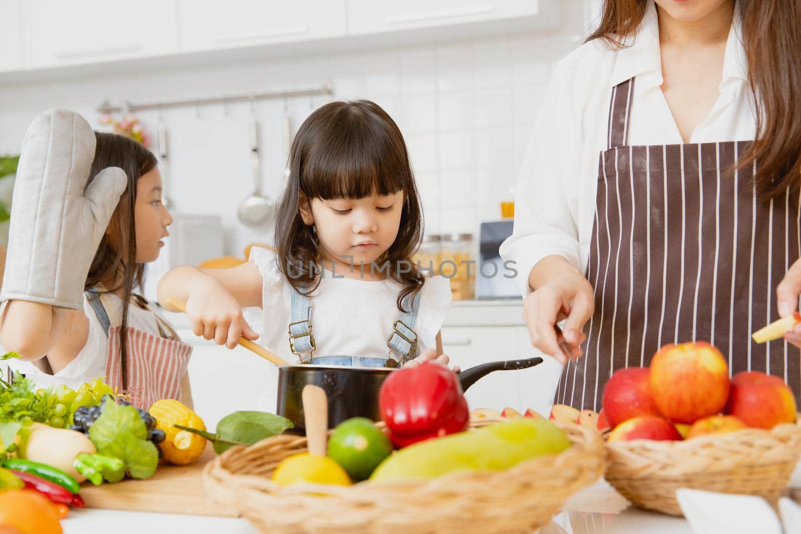 Little girl childs enjoy playing cooking with mom and older sister together at home kitchen holiday by qualitystocks