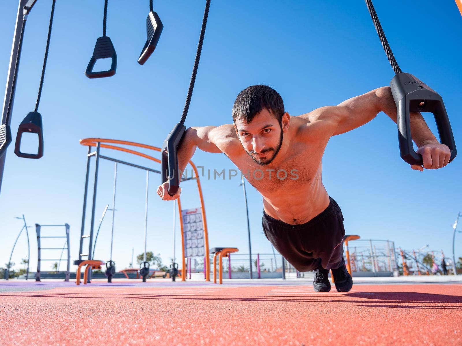 Shirtless man doing loop exercises outdoors. by mrwed54